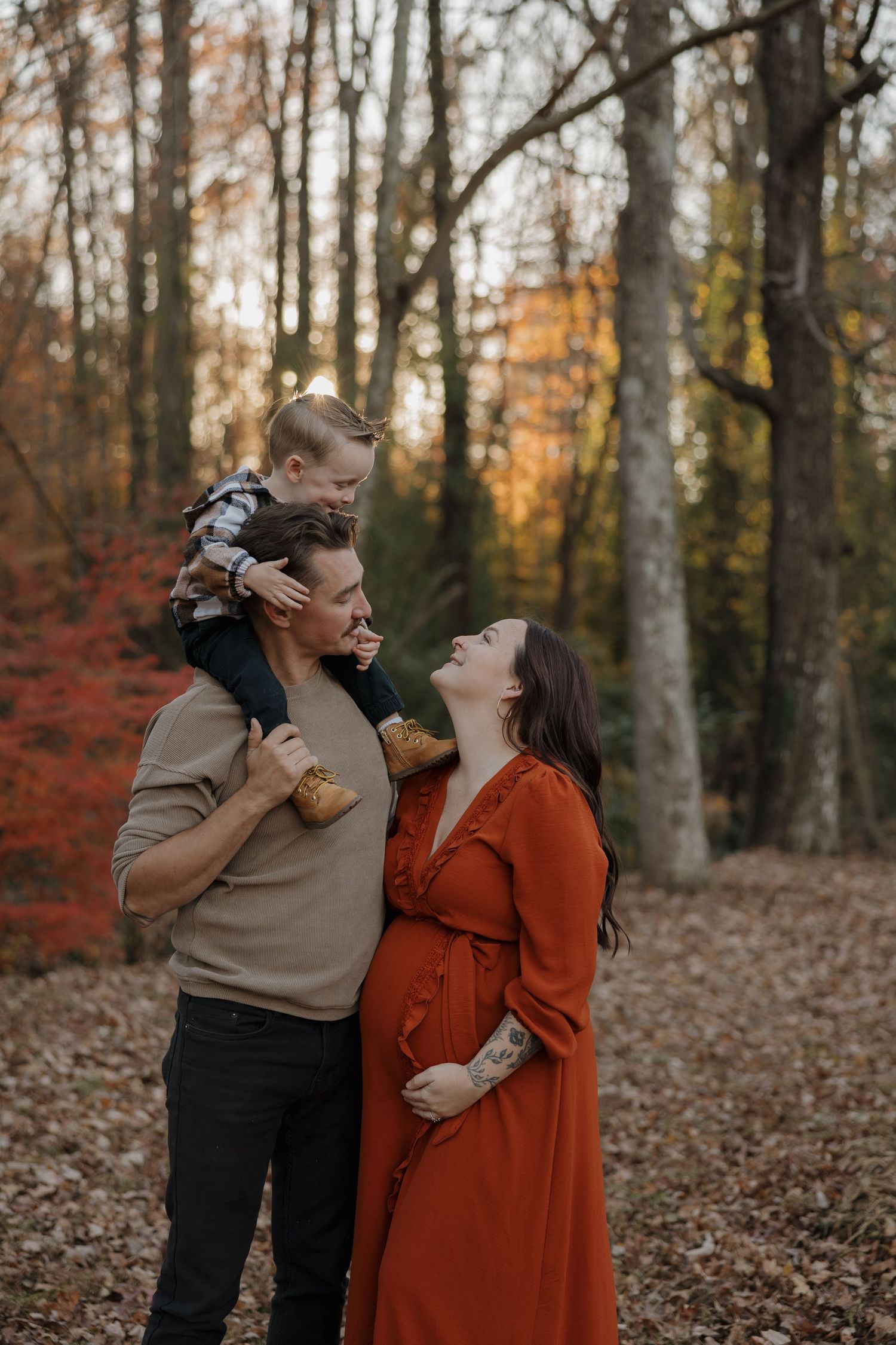 A couple laughs together in a forest filled with autumn leaves and warm fall colors.
