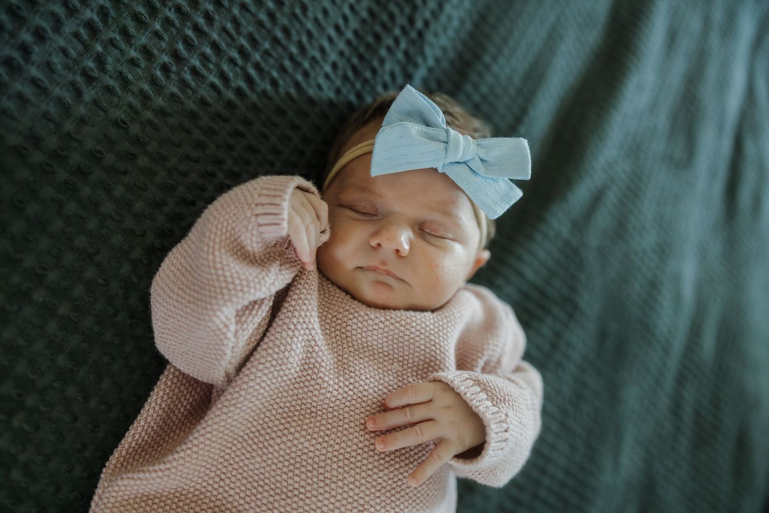 A sleeping newborn baby wrapped in a pink polka dot swaddle blanket rests peacefully against a dark background.
