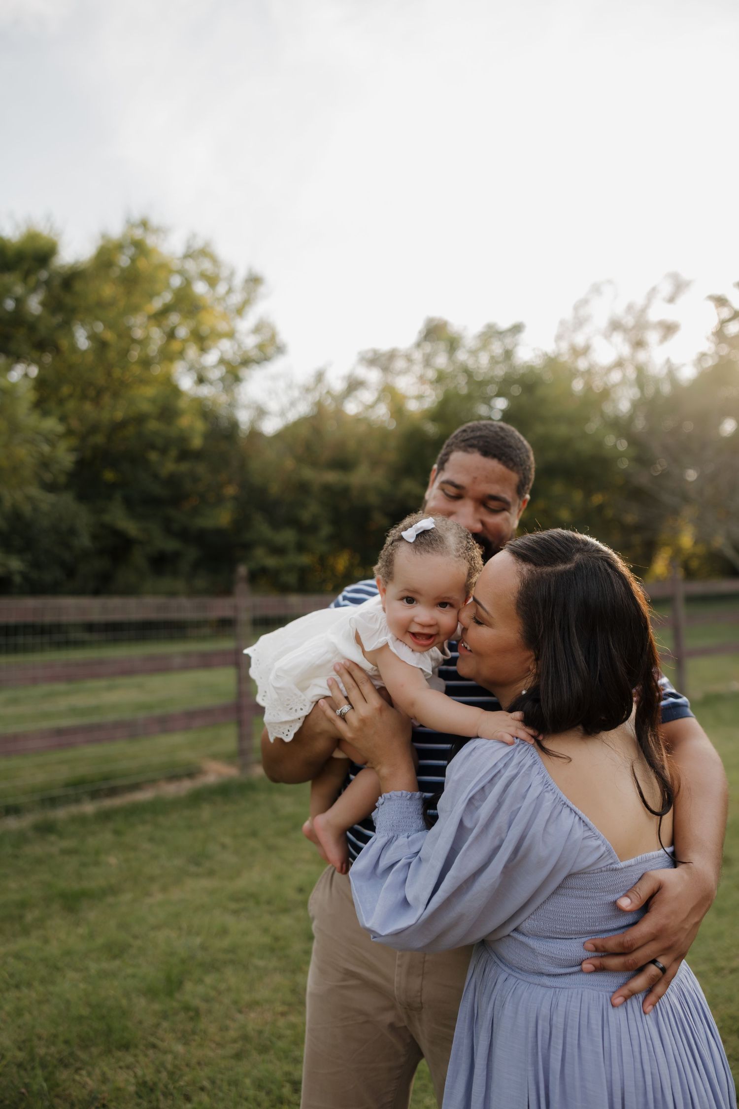 A family shares tender moments together in a grassy field during golden hour.