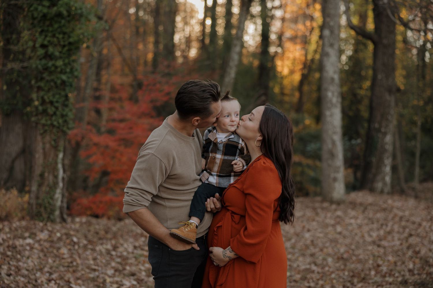 A couple shares an intimate moment in a forest with autumn leaves during sunset.