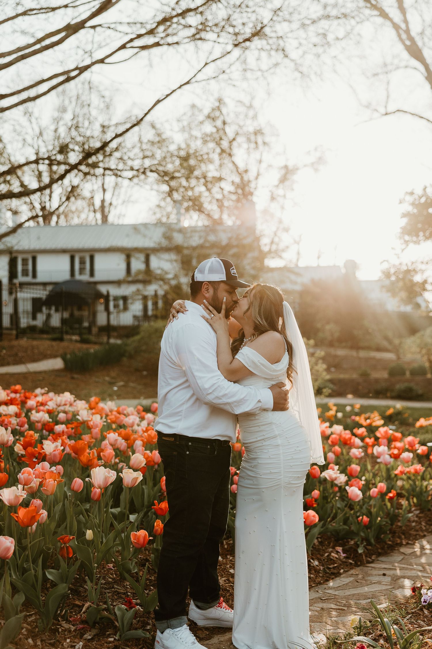 Wedding couple embraces in garden with blooming orange and pink tulips at sunset.