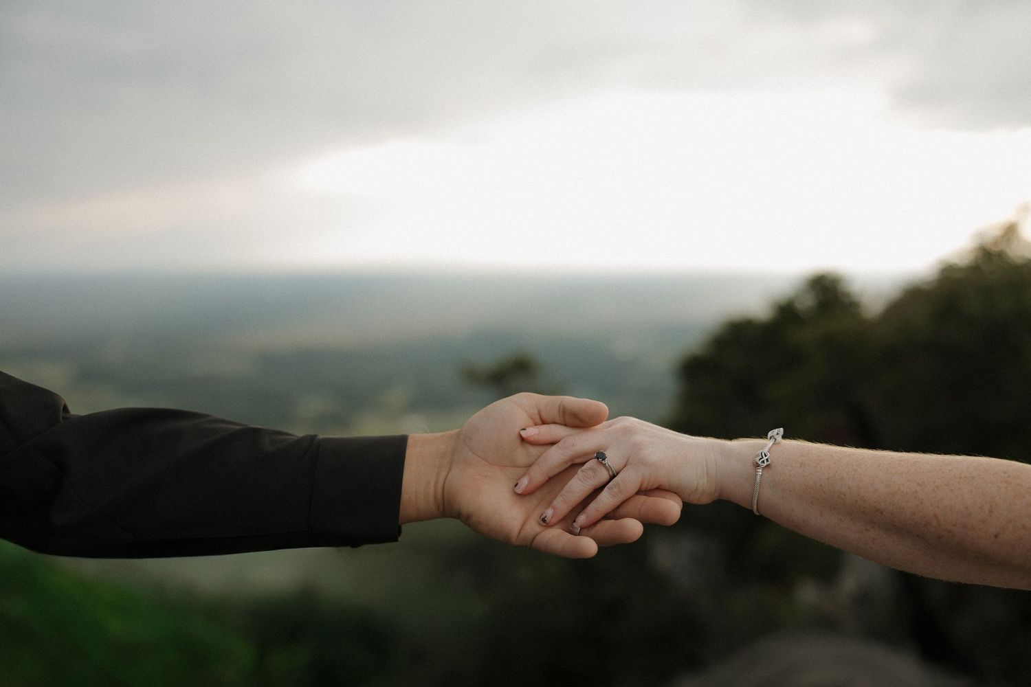 Close-up shot of two hands clasping together with a blurred mountainous landscape in the background.