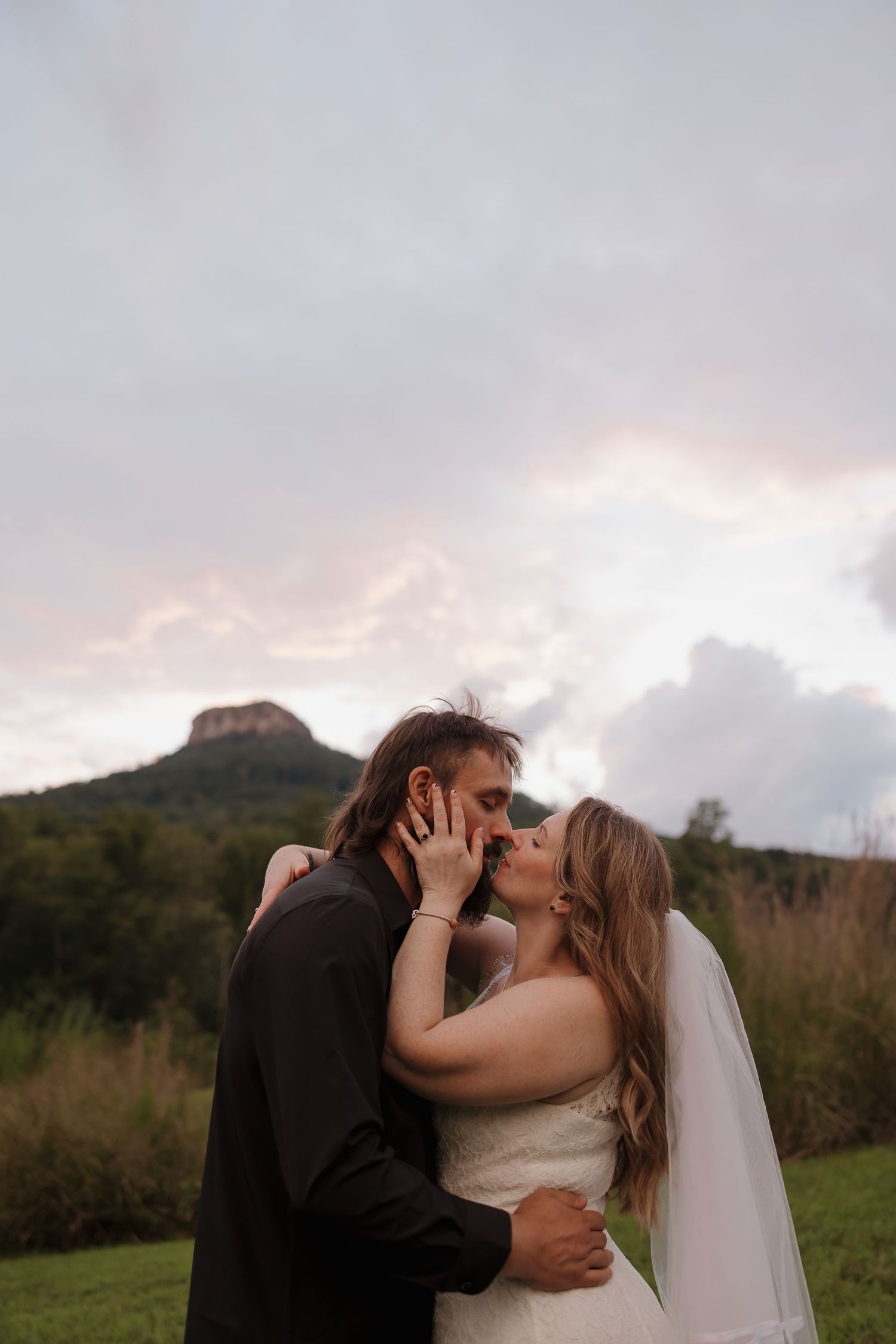 A romantic moment captured between newlyweds against a mountainous backdrop during sunset.