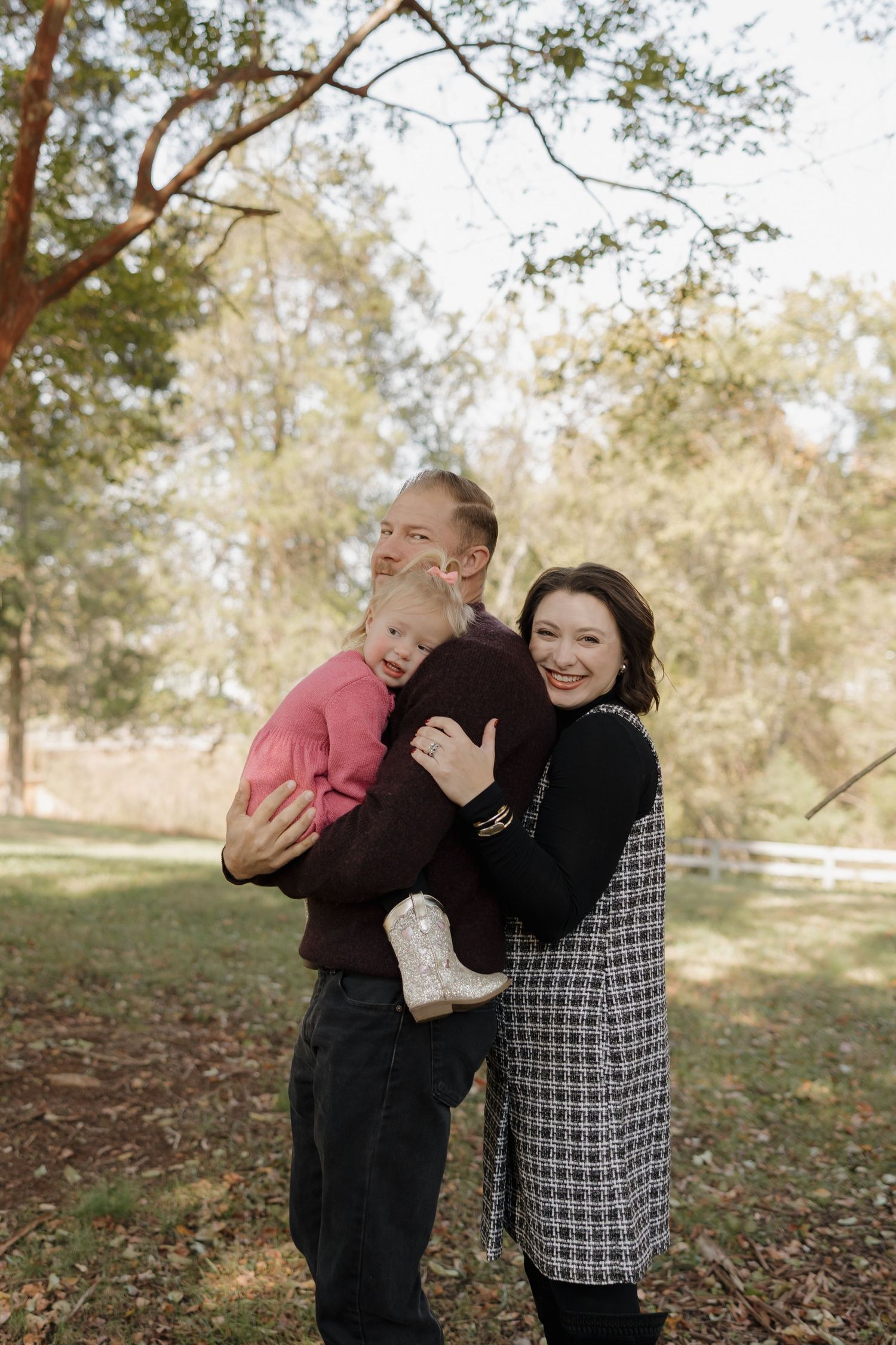 A family shares joyful laughter together during an outdoor autumn photoshoot in a wooded setting.