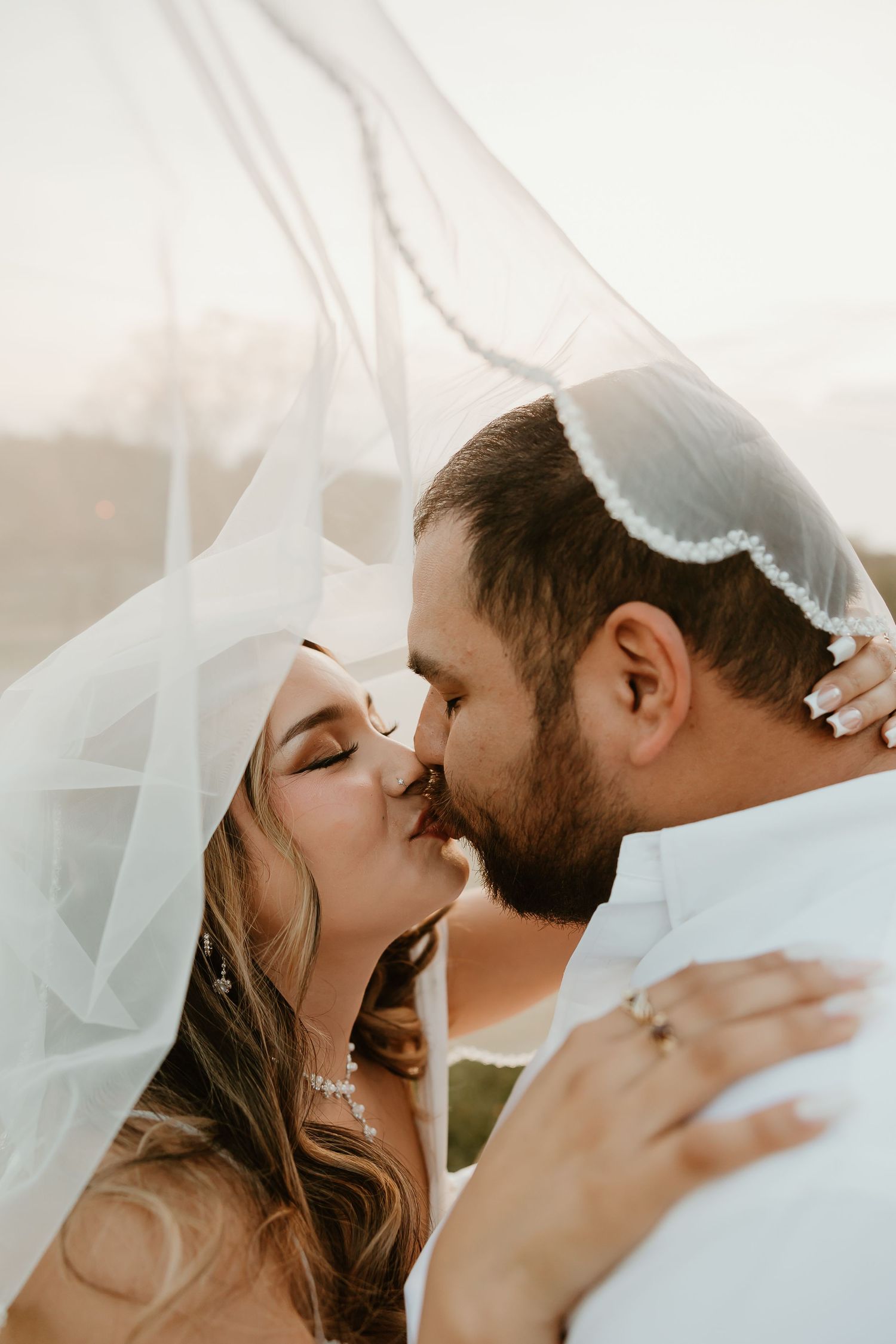 Intimate wedding couple portrait with flowing veil in soft natural light.