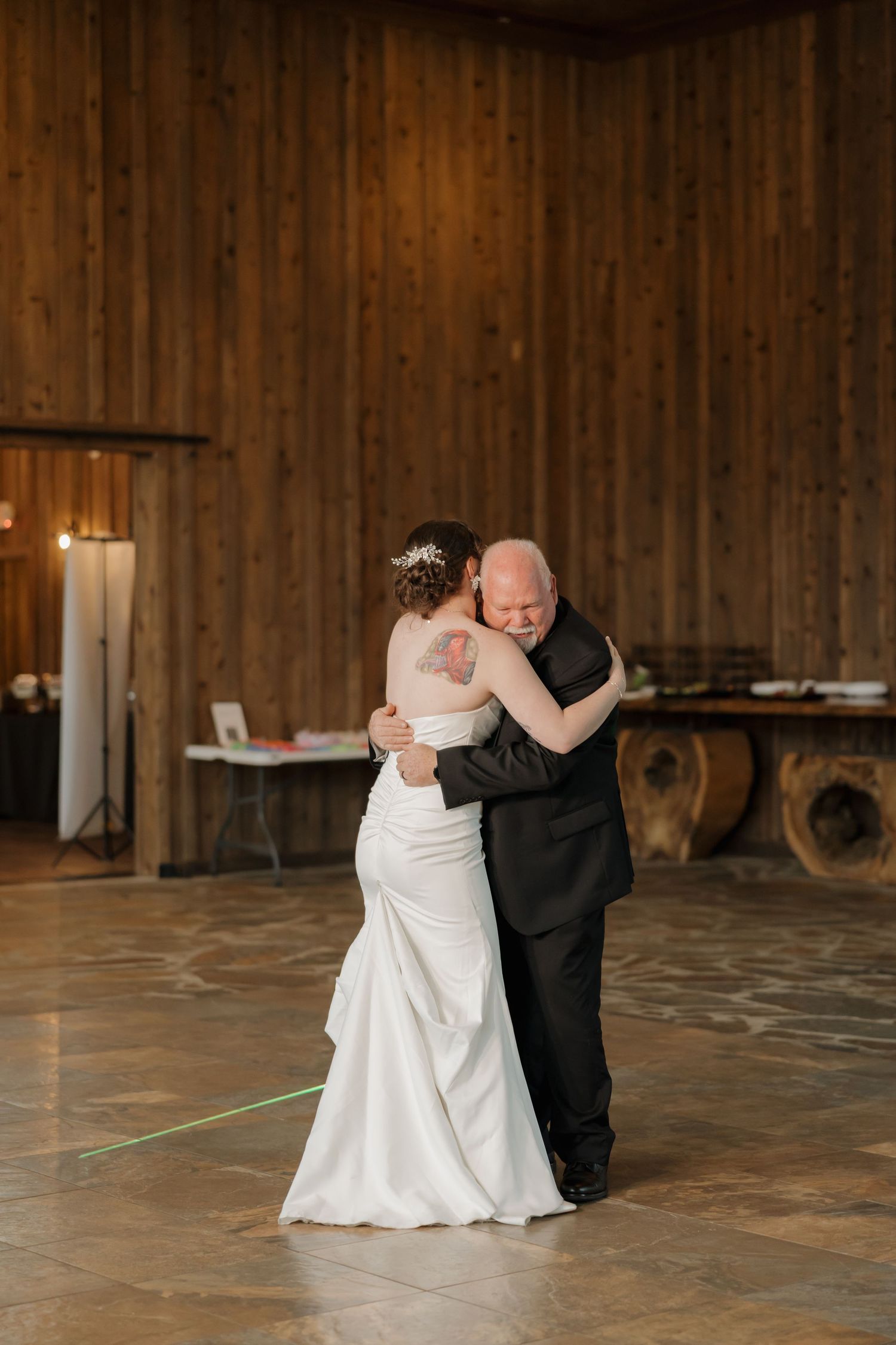 Bride and father share an emotional first dance in a rustic wood-paneled barn venue during wedding reception.