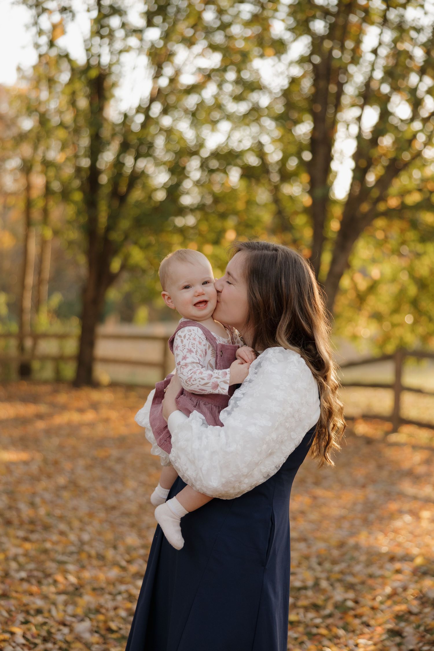 A tender moment between parent and baby during golden hour in an autumn park with fallen leaves scattered on the ground.