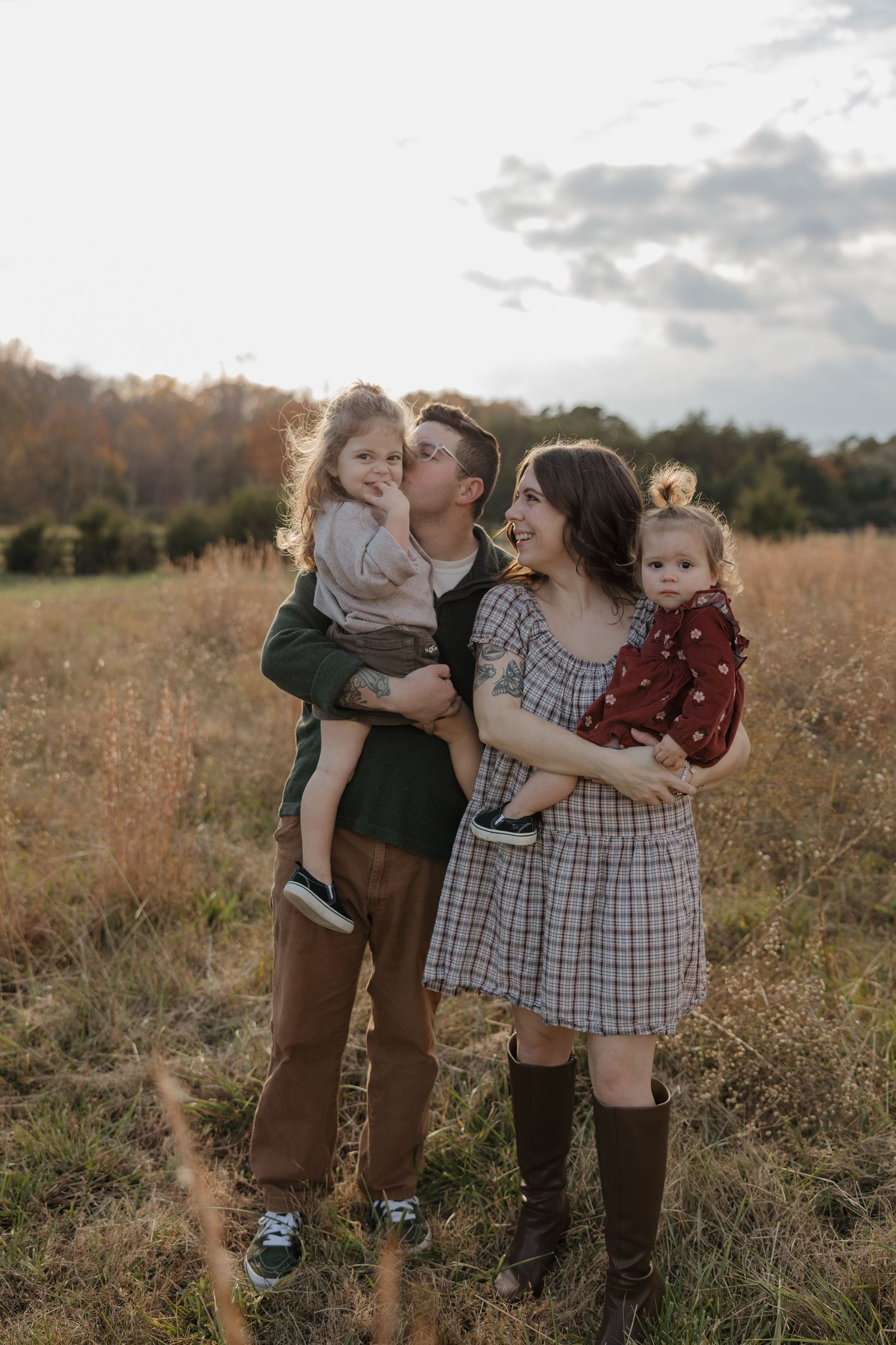 A family stands together in a golden autumn field at sunset with tall grass surrounding them.