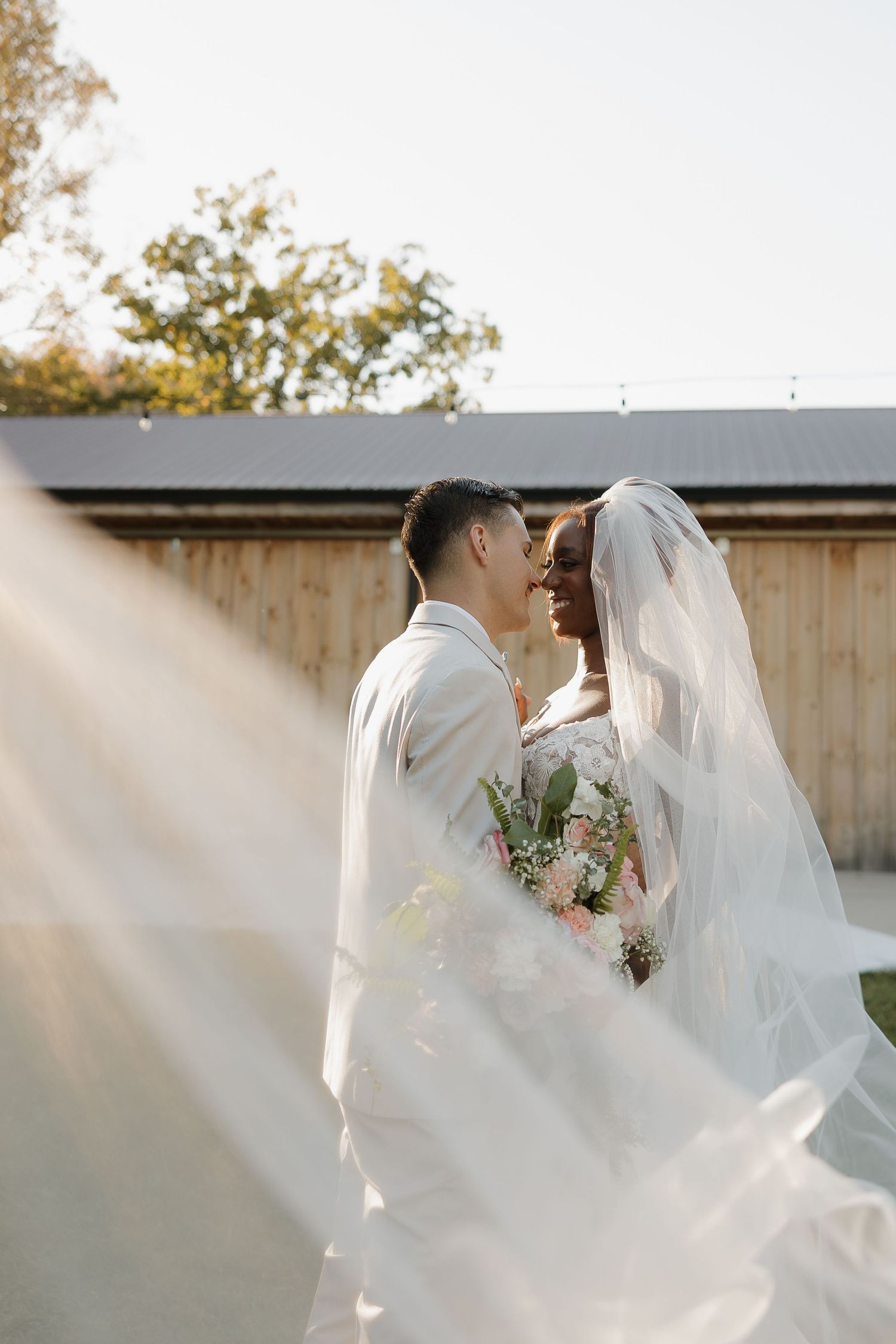 Romantic wedding portrait against wooden barn in soft natural light.
