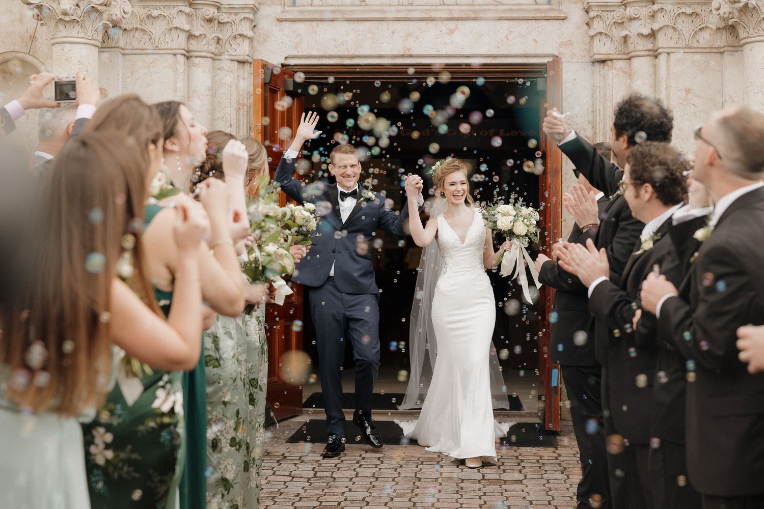 Wedding guests throw confetti outside a stone church during an exit celebration.