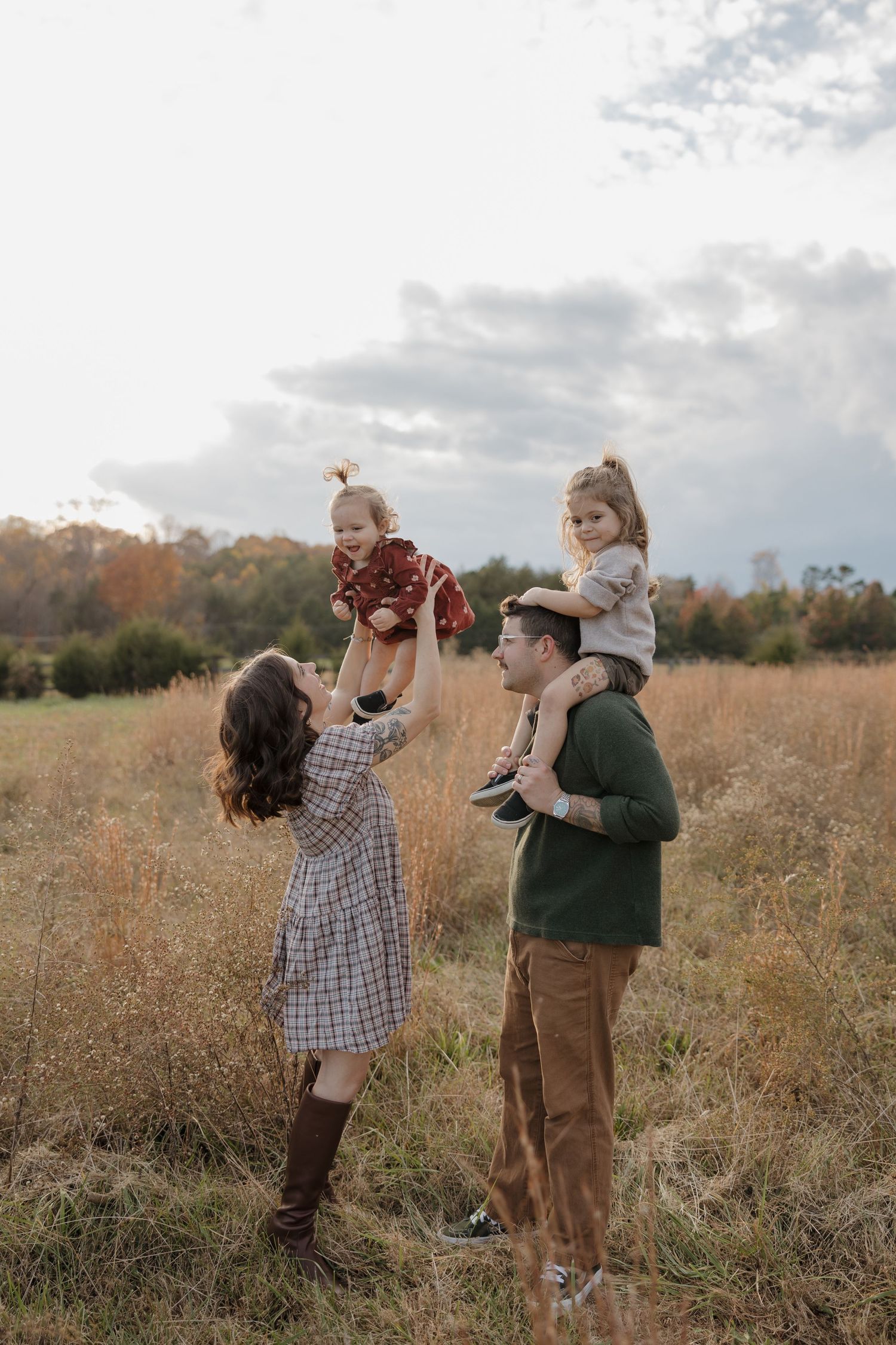 Two children play together in a golden autumn field during sunset with tall grass and trees in the background.