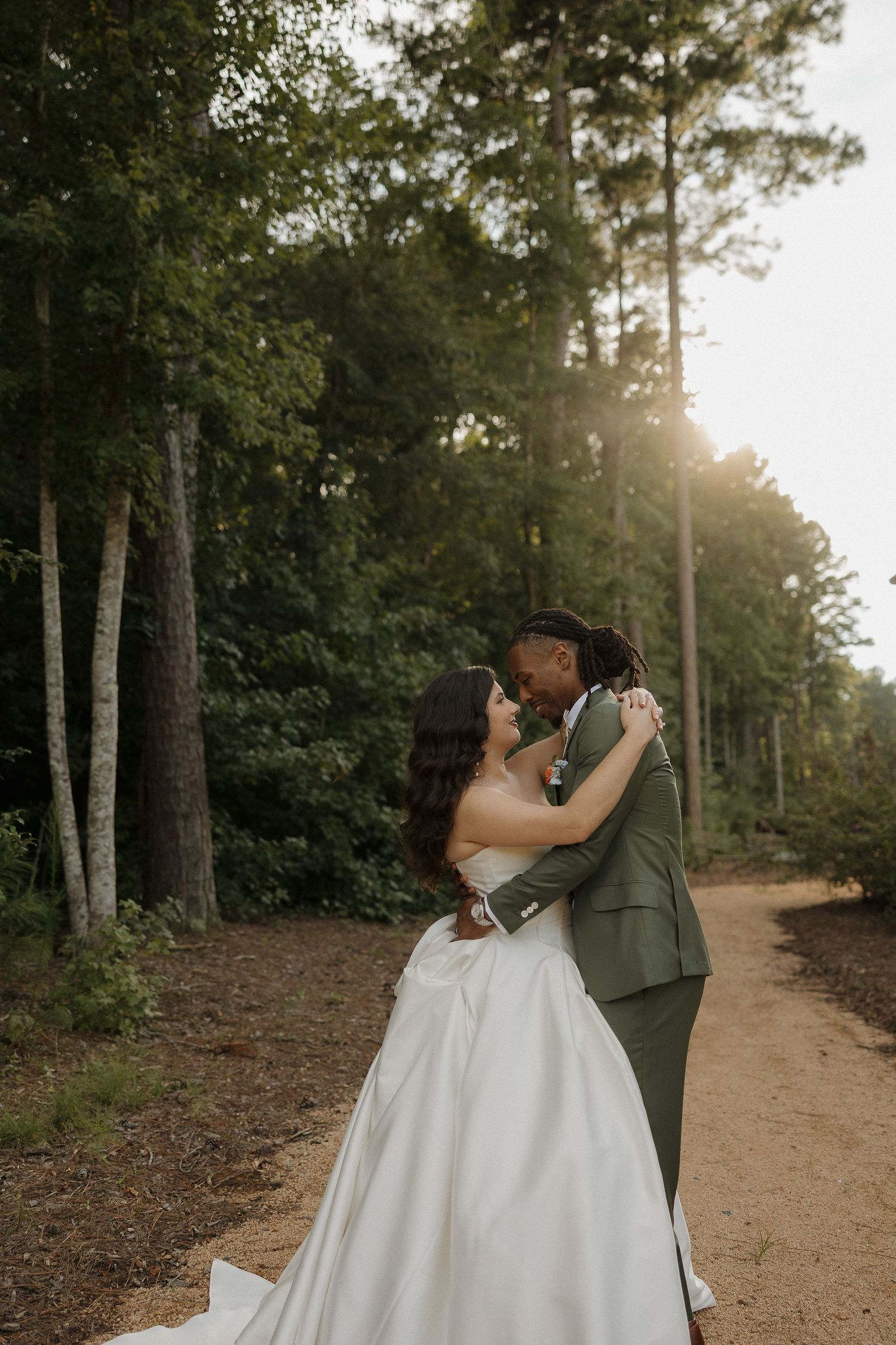 A romantic sunset wedding portrait of a couple embracing on a forest path.