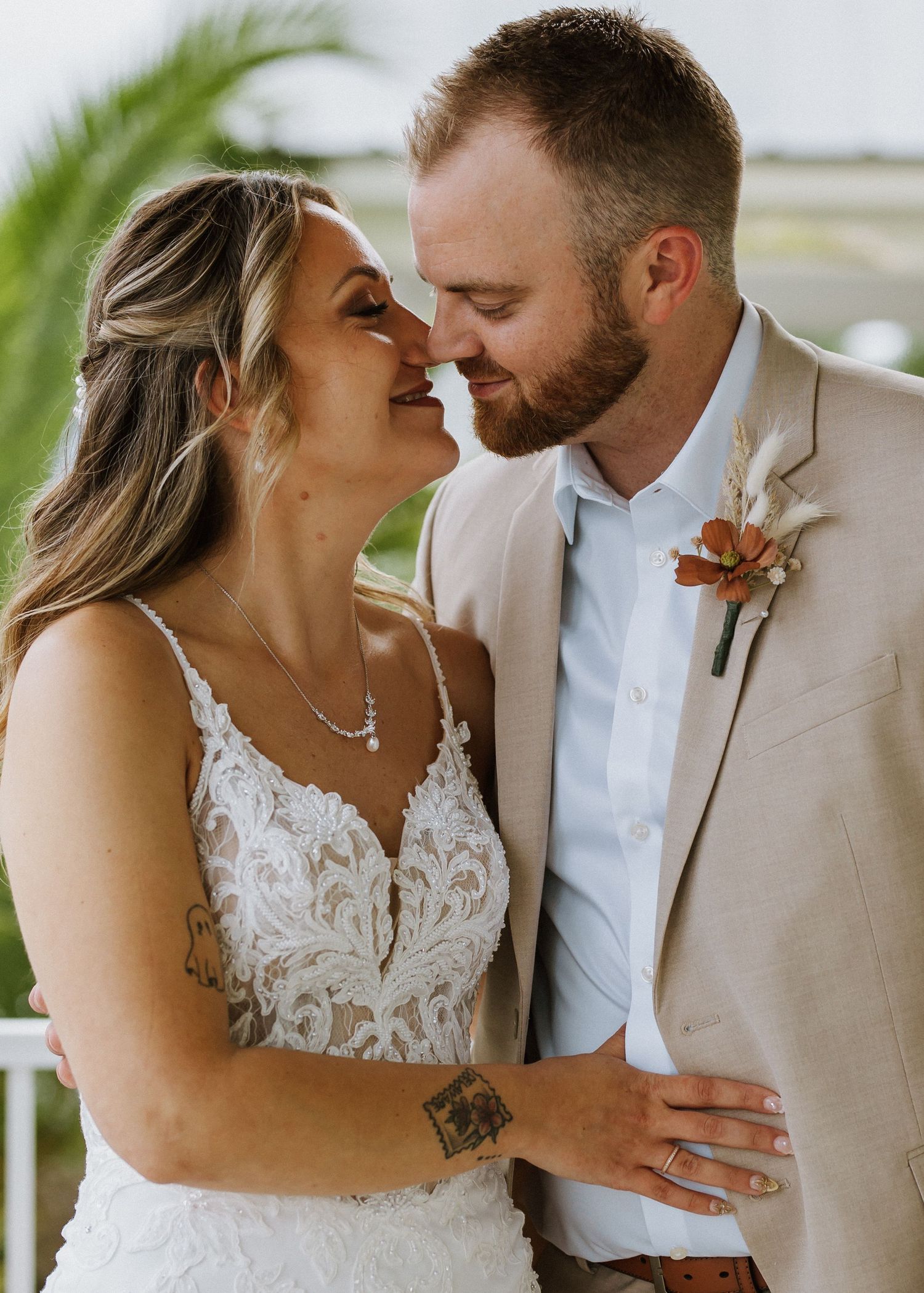 A smiling bride and groom in a tan suit share a romantic moment during their outdoor wedding celebration.