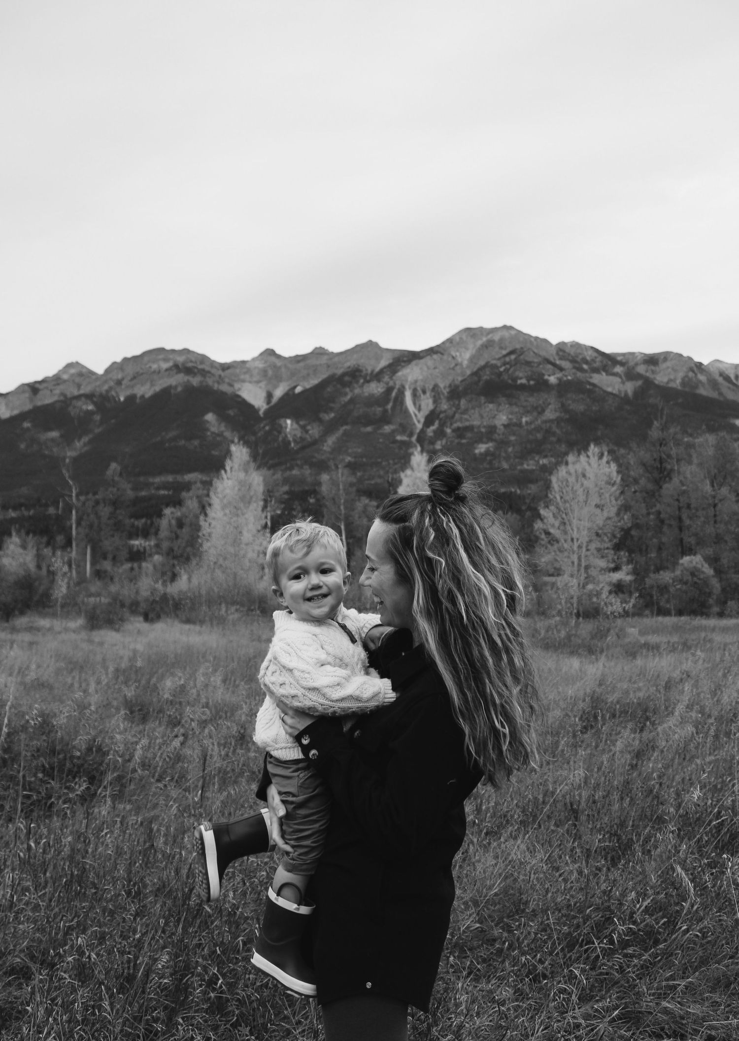 Black and white portrait of a tender moment in a mountain meadow with dramatic peaks in the background.