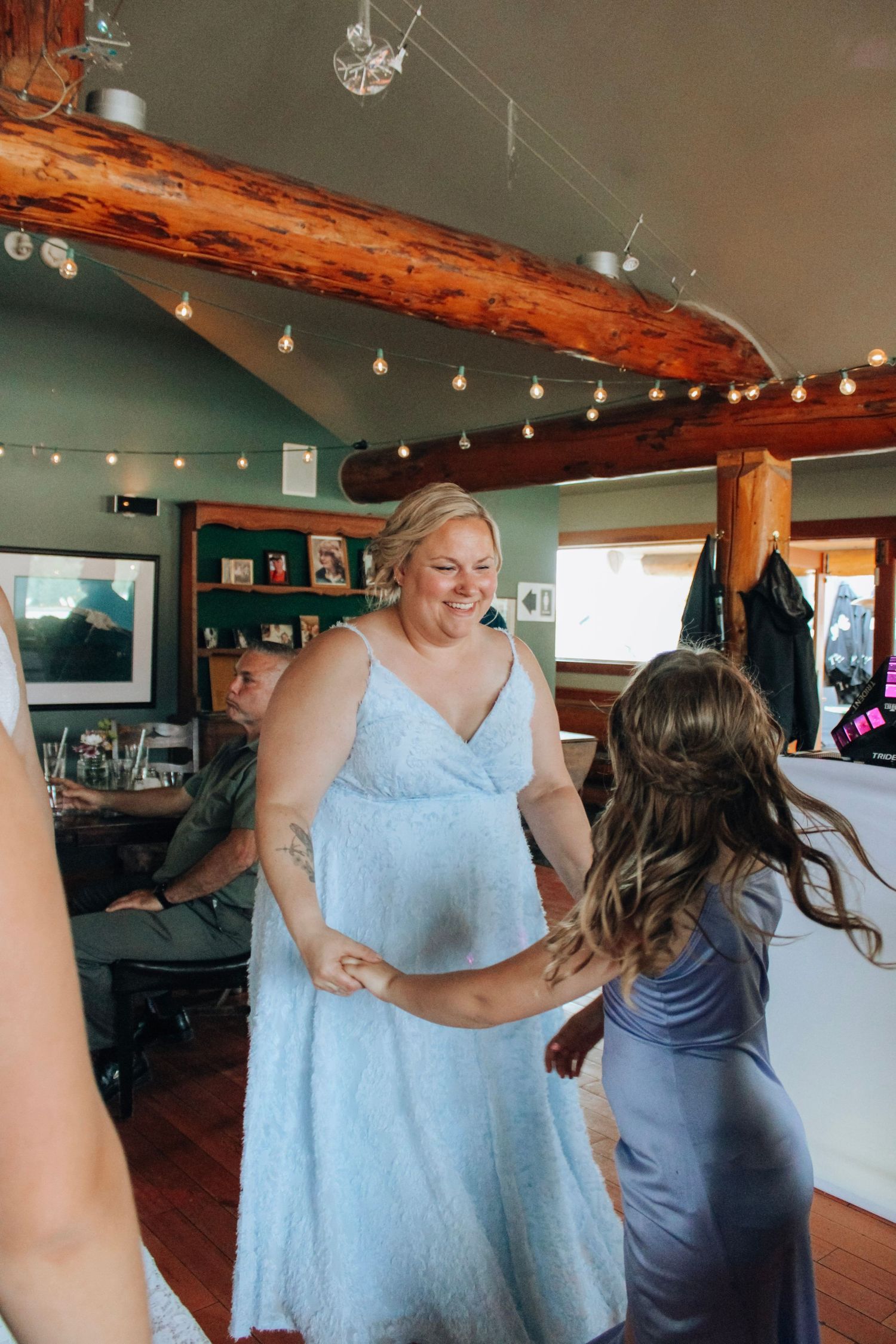 Wedding party members in light blue and gray dresses dancing at an indoor reception.