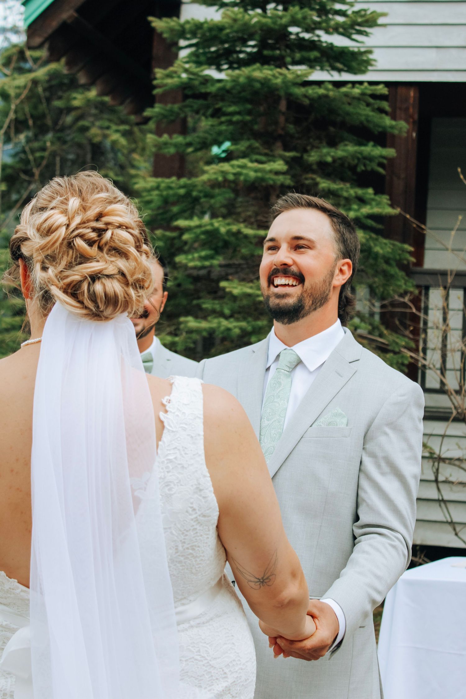 A couple shares a joyful moment together outdoors with evergreen trees in the background.