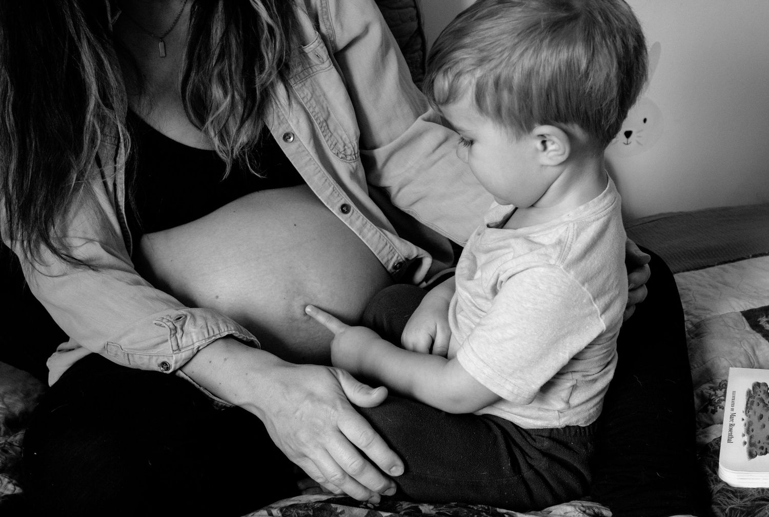 A black and white image shows a woman holding a young child in her lap, creating a tender, intimate moment.