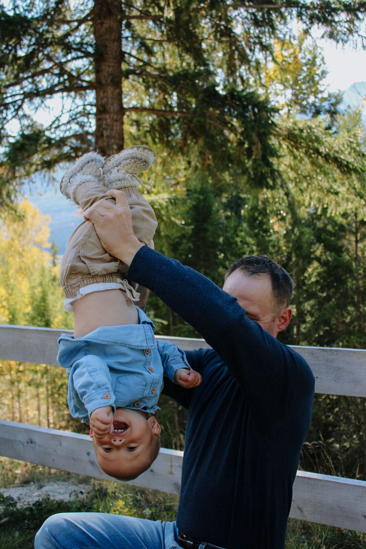 Playful moments captured by a wooden fence with autumn foliage in the background.
