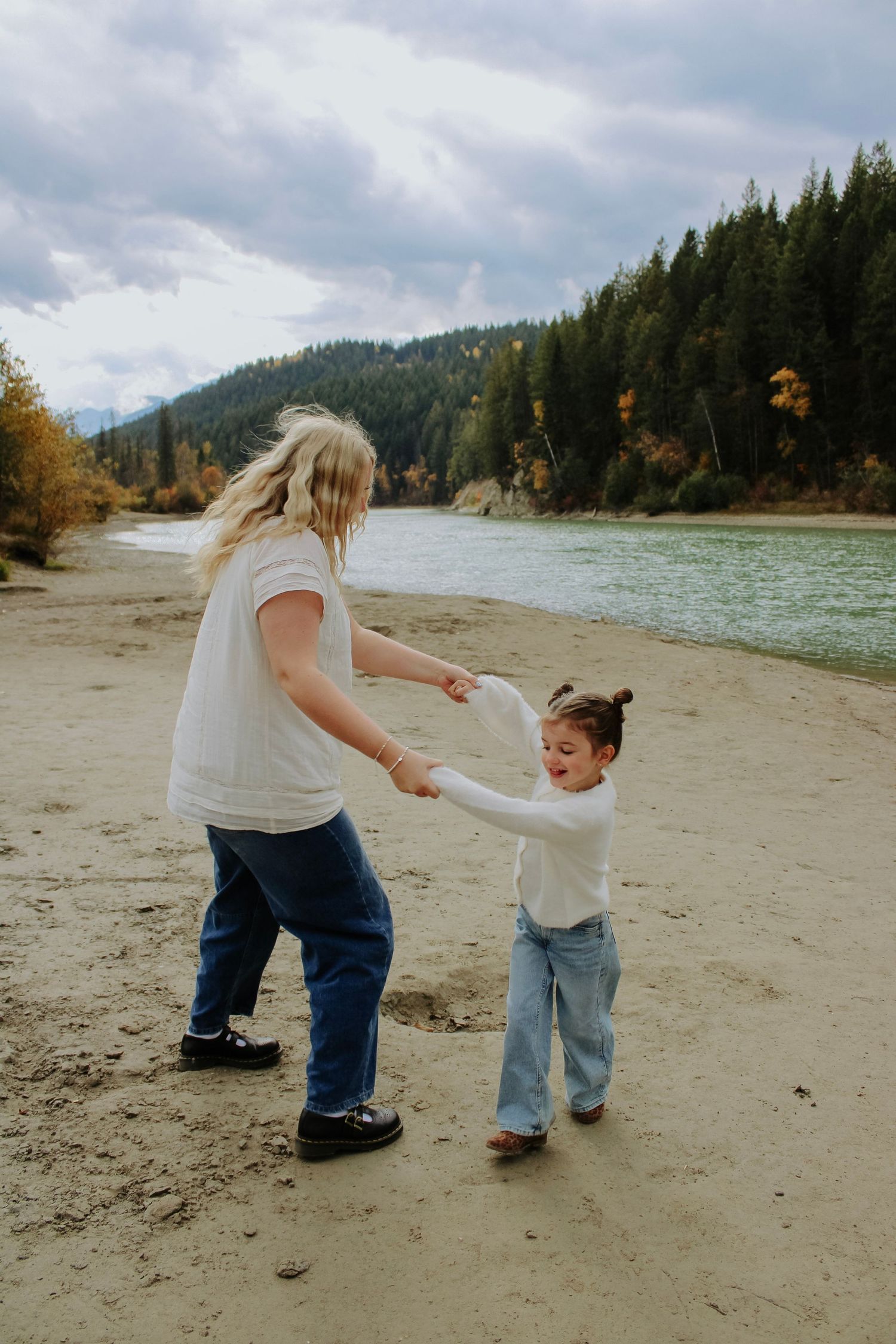 Candid moments on sandy beach with forest and mountains in background.