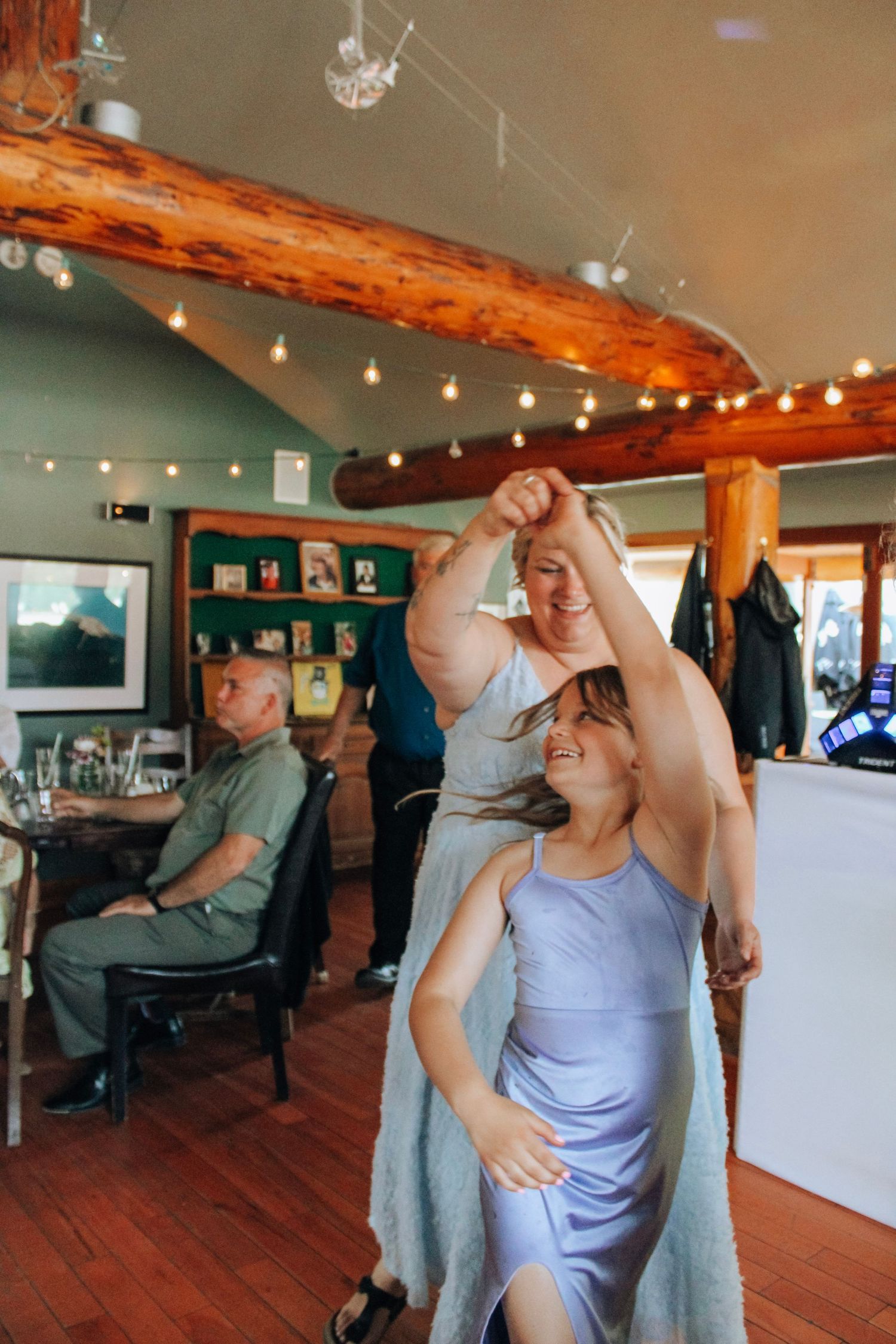 Wedding party dancing and celebrating in a rustic venue with wooden beams and string lights.