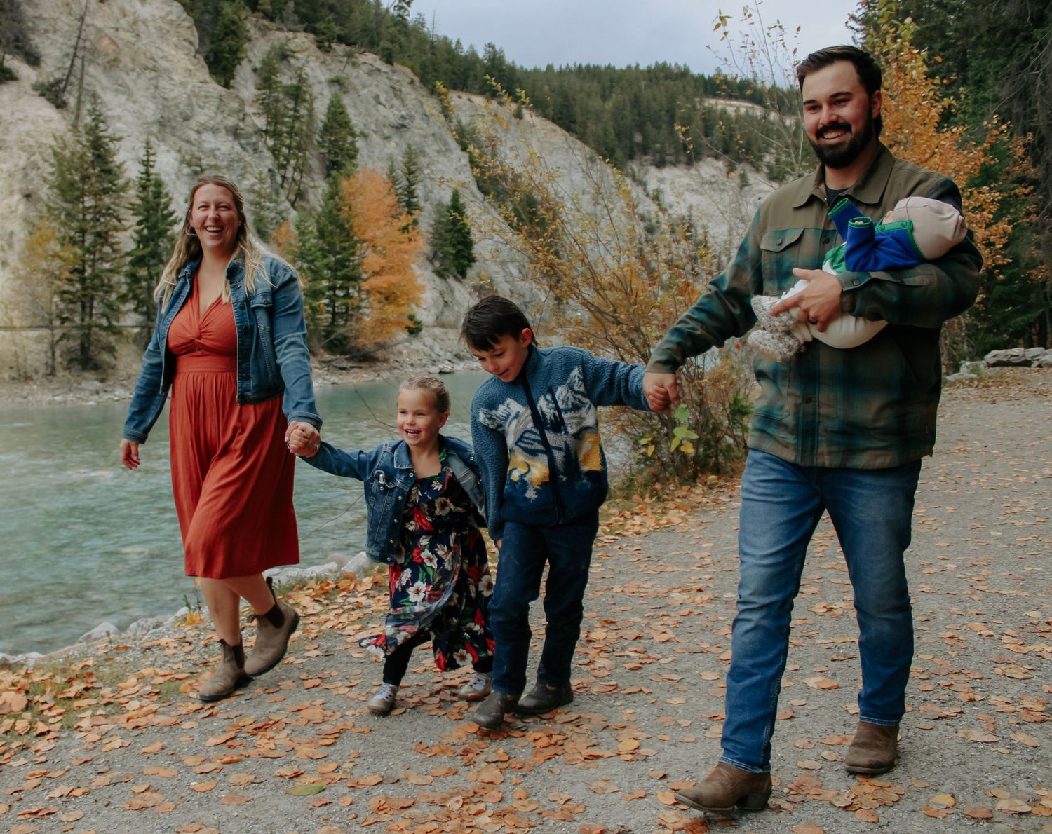 Family playing together on an autumn path surrounded by mountain scenery.