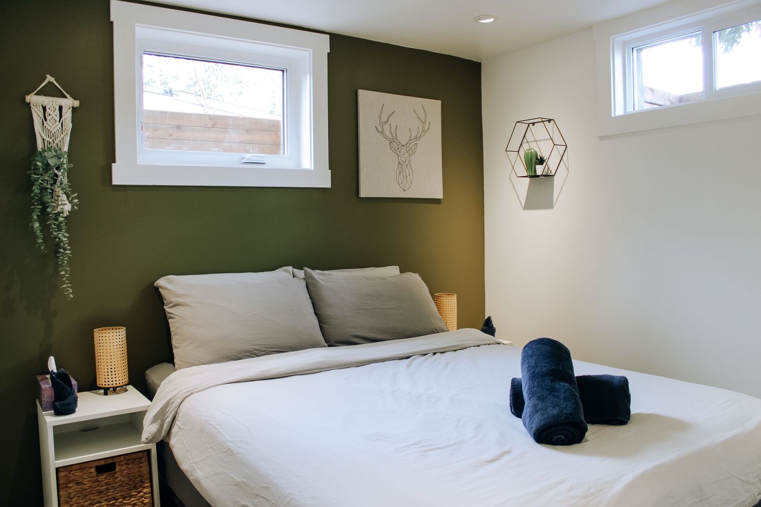Minimalist bedroom with green accent wall, white bedding, and high windows letting in natural light.