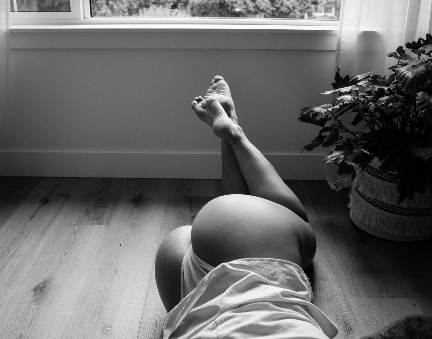 Minimalist black and white photo of person lying near window in natural light.