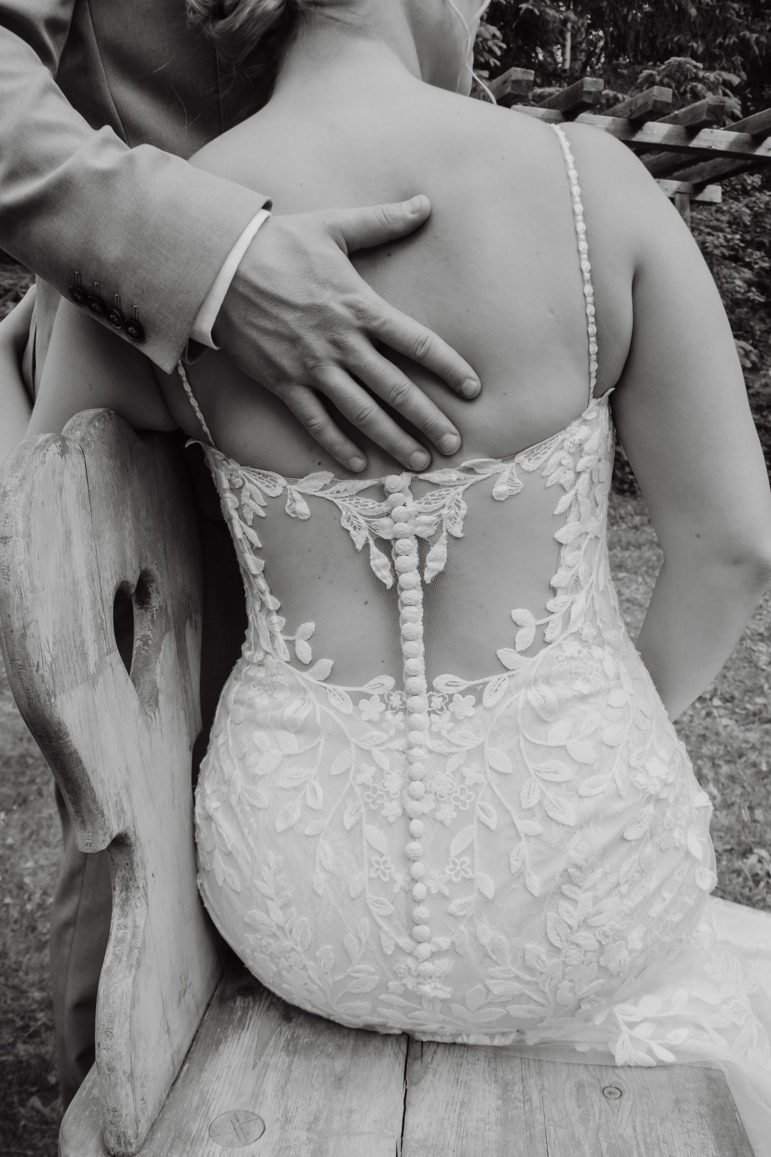 Black and white photo of bride in lace back wedding dress with groom's hand on her back.