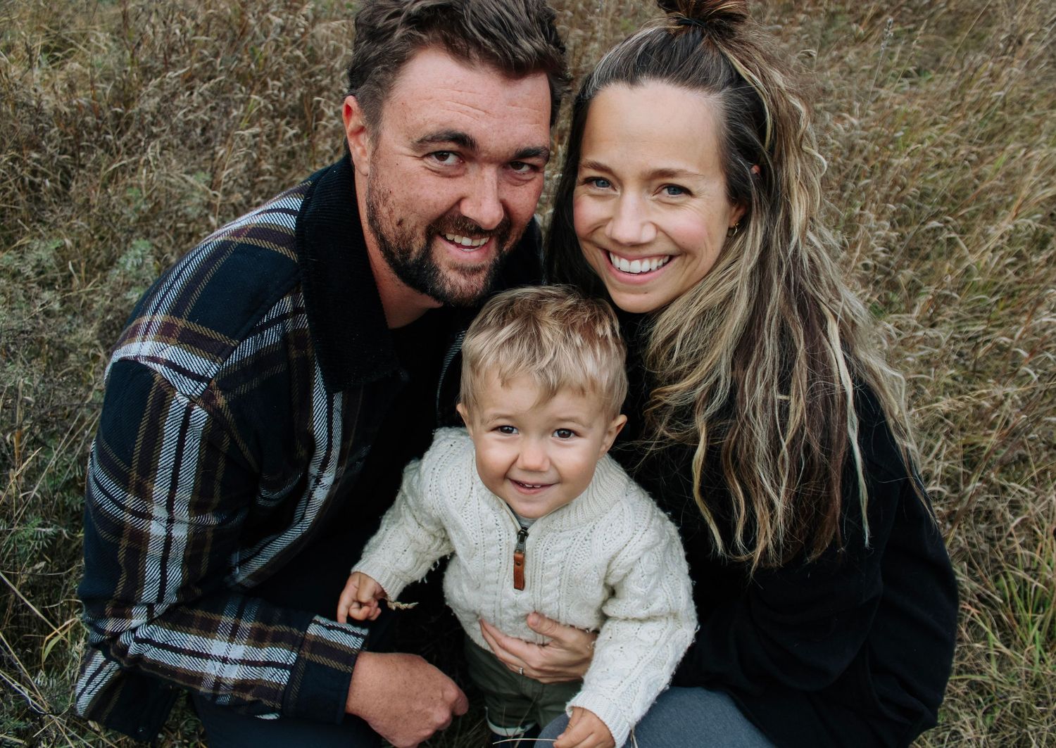 Candid family portraits taken in tall grass with natural outdoor lighting.