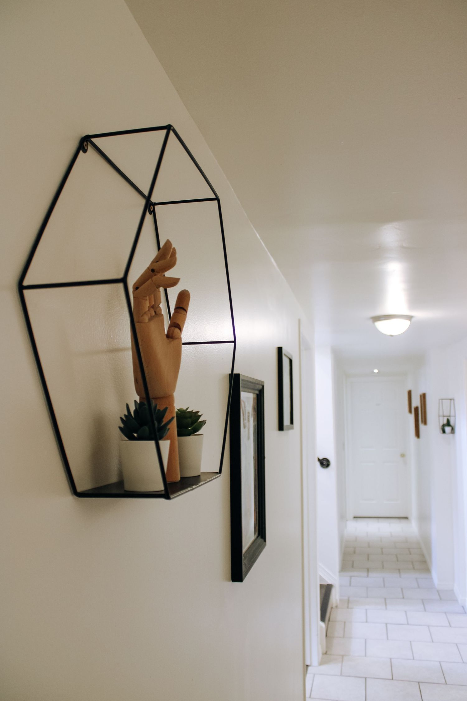 White hallway with geometric black wall mirrors and modern lighting fixtures.