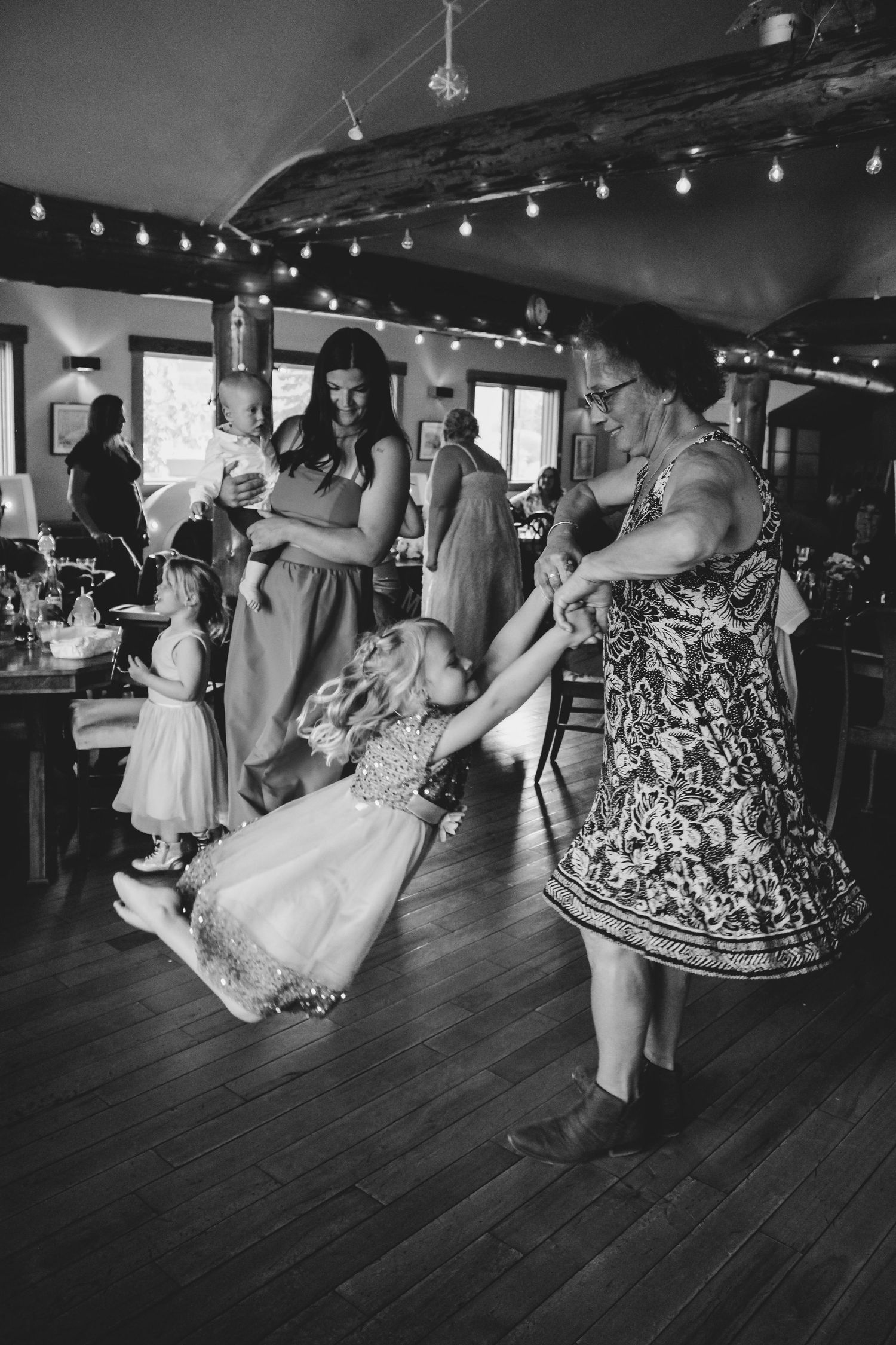 Black and white photo of people dancing in white and patterned dresses at an indoor venue.