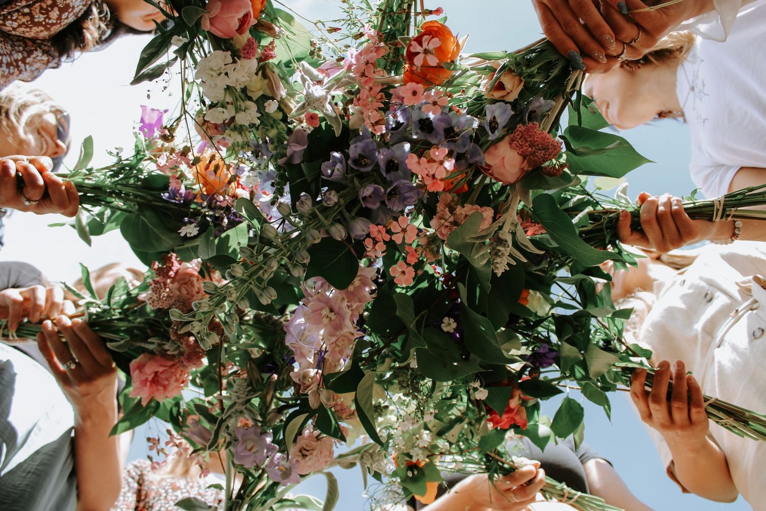 A stunning upward view of people holding a lush floral bouquet with pink, purple, and white blooms outdoors.