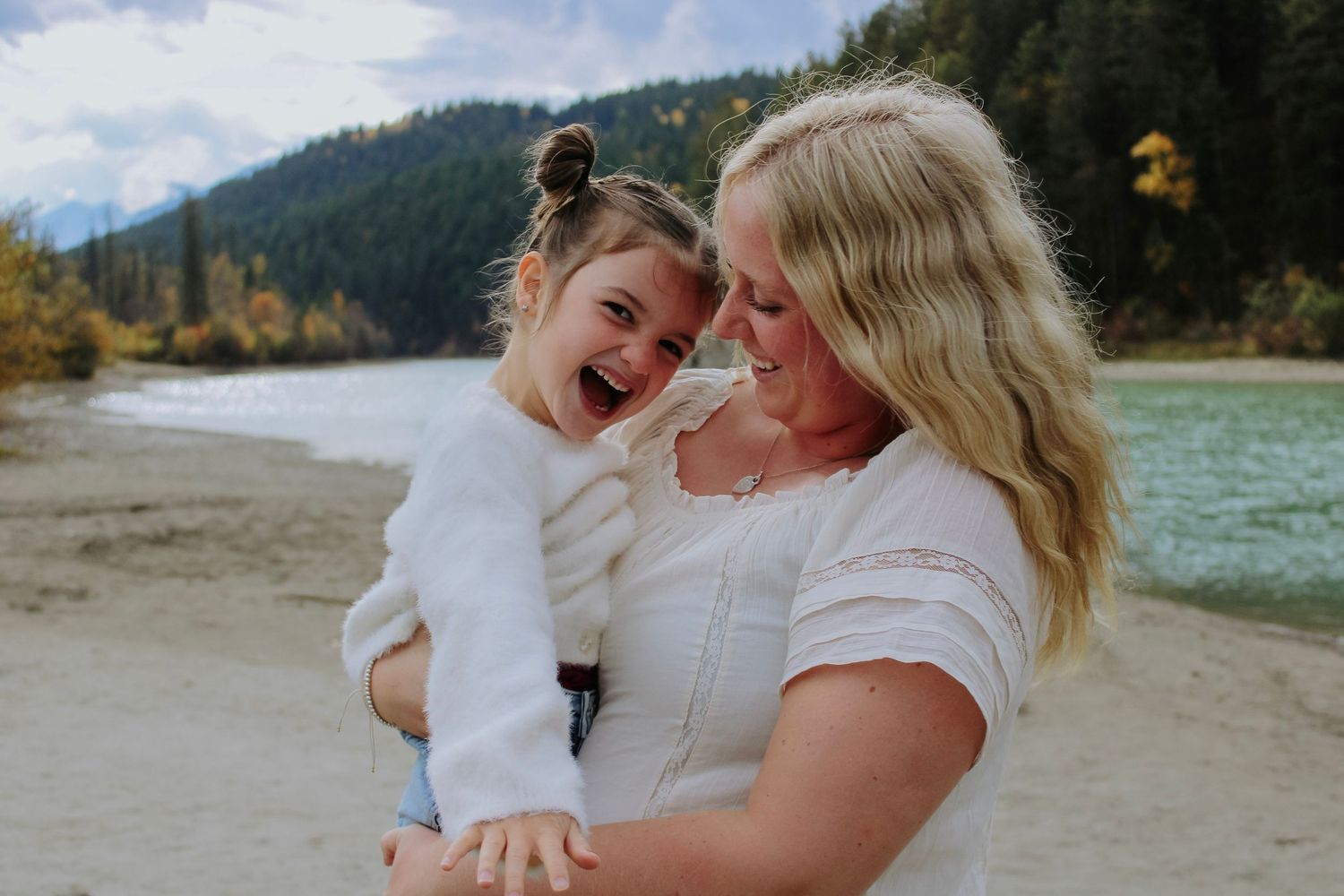 Joyful moments shared on beach with mountains and forest in background.