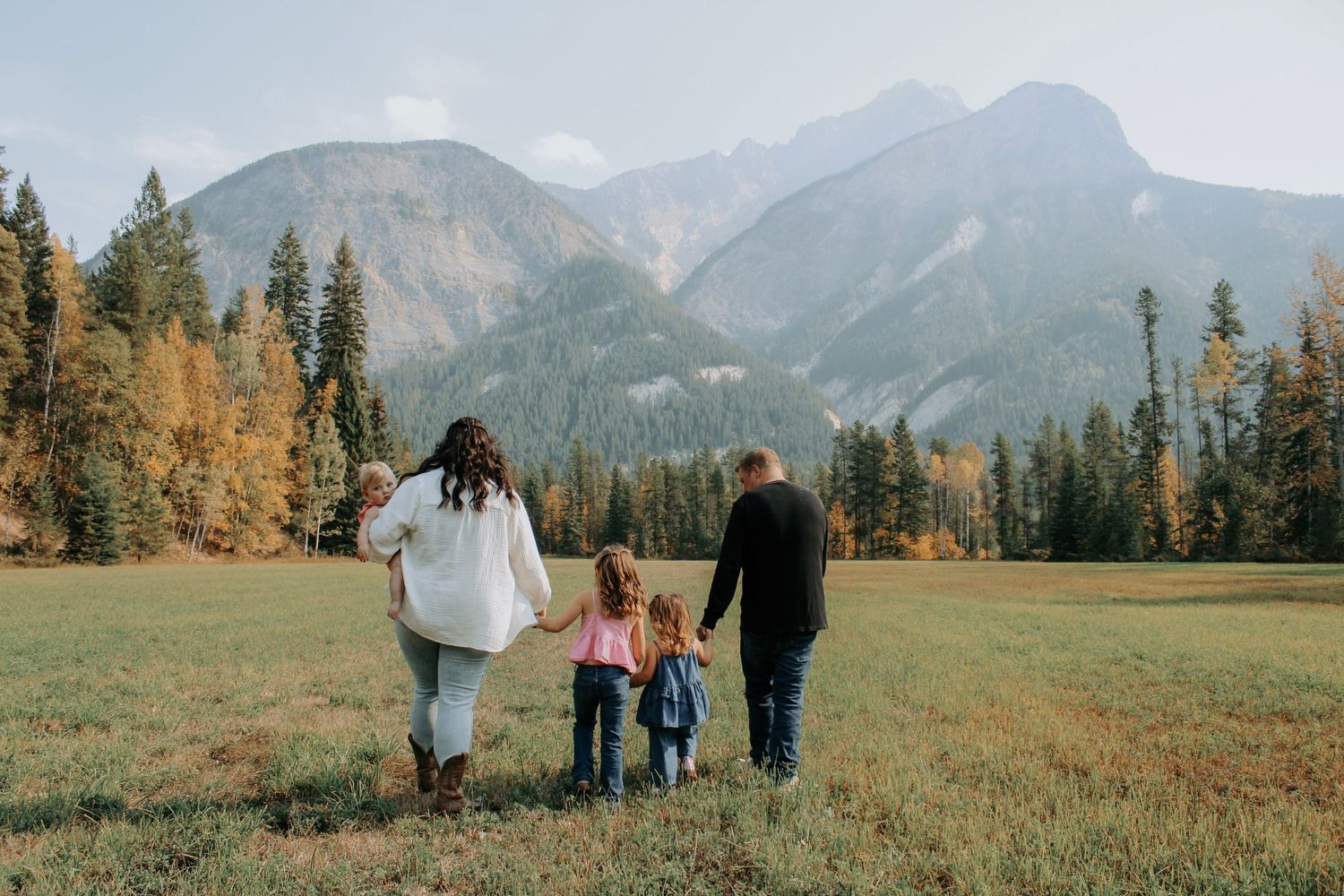 Scenic mountain landscape with family silhouettes walking through meadow at sunset.