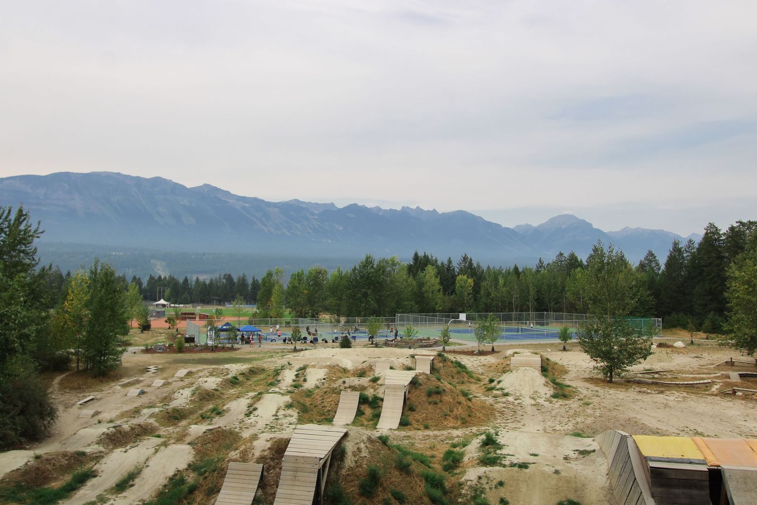 Aerial view of a mountain bike dirt jump park surrounded by trees with scenic mountain range backdrop.