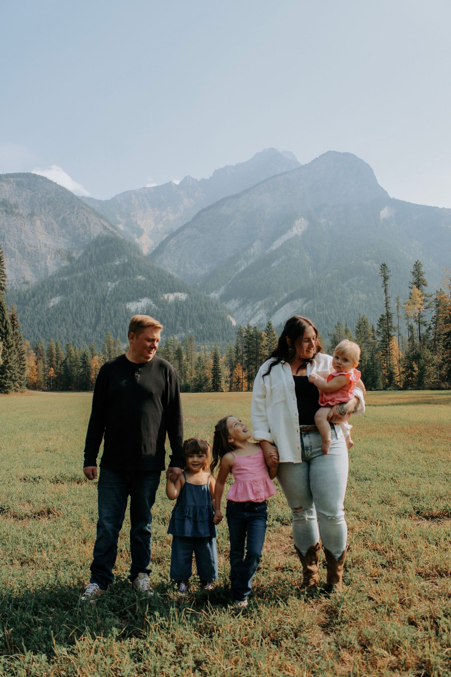 Family group walking together across mountain meadow with dramatic peaks in background.