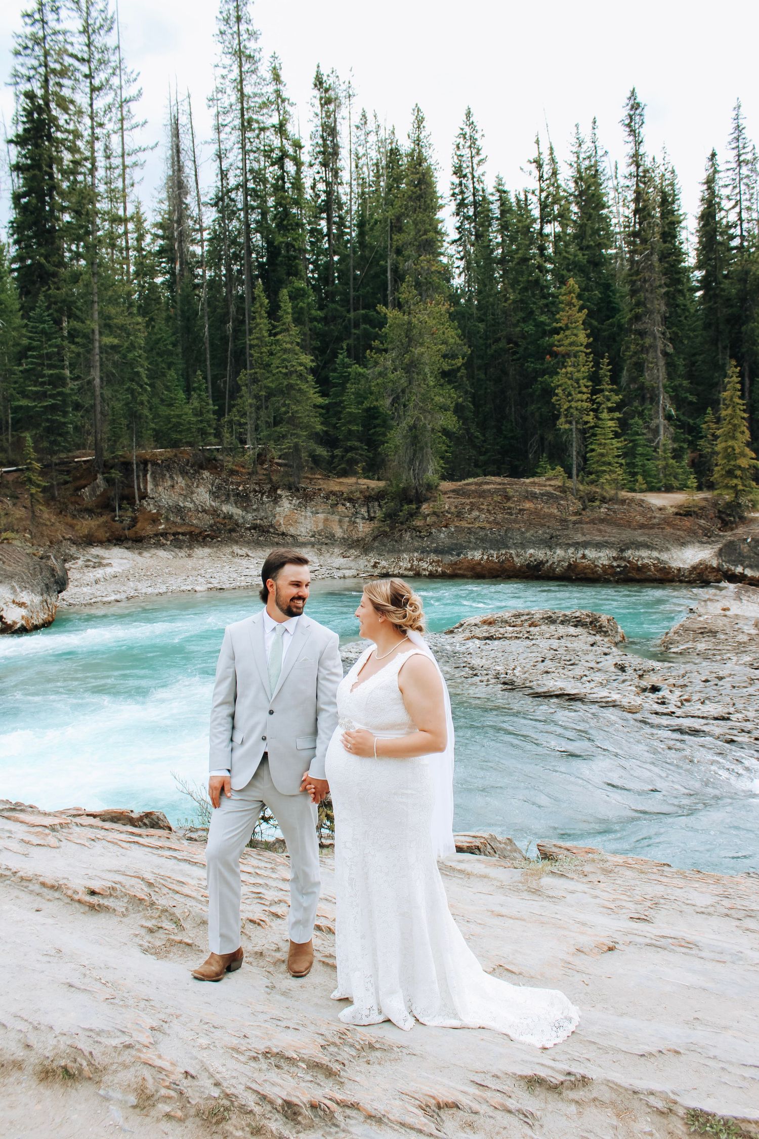 Bride and groom sharing joyful moments by turquoise mountain river.