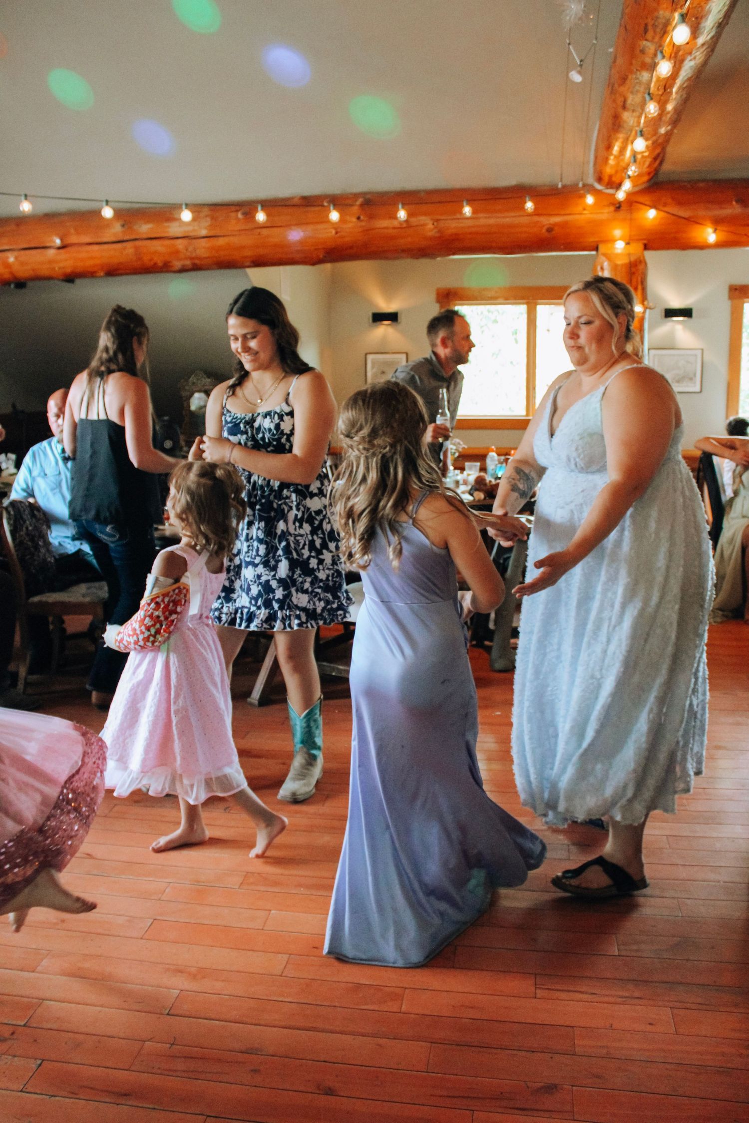 Wedding guests dancing on a wooden floor under warm lighting in a rustic reception venue.