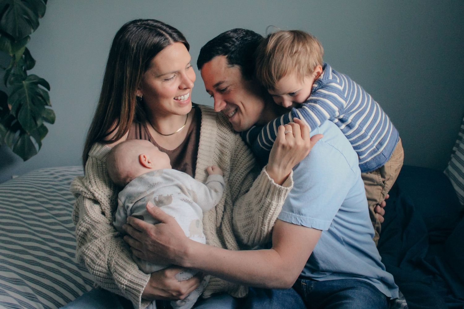 Happy family with newborn baby and toddler sharing a tender moment together on a bed at home.
