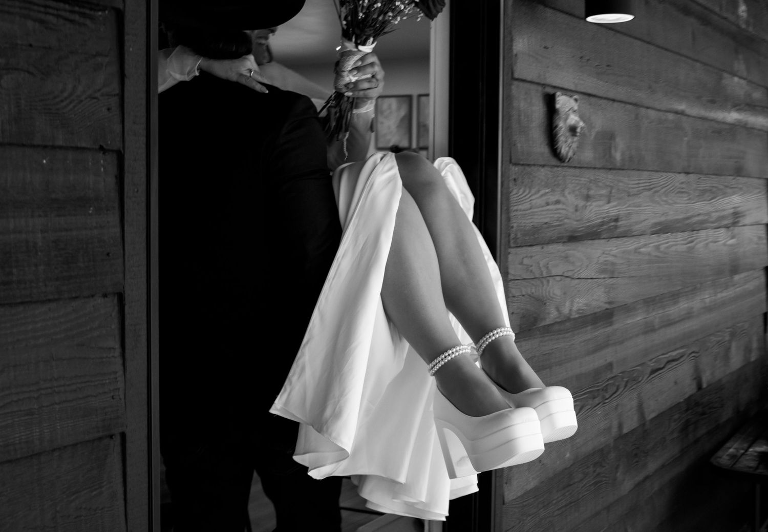 A black and white photo shows a person in a white dress walking up wooden stairs in dramatic lighting.