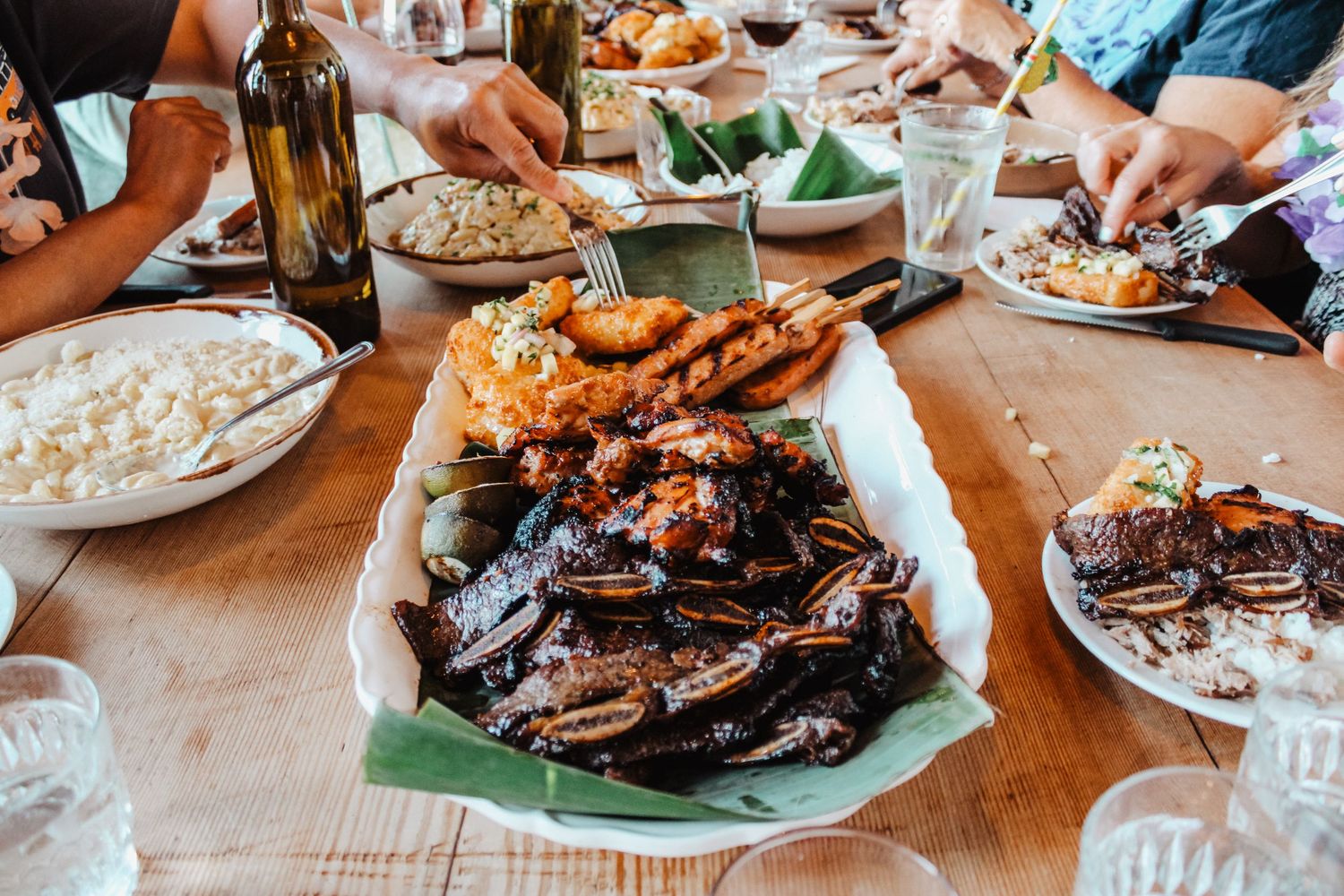 A festive outdoor dinner table spread with Filipino dishes including mussels, fried shrimp, and grilled meat shared among friends.