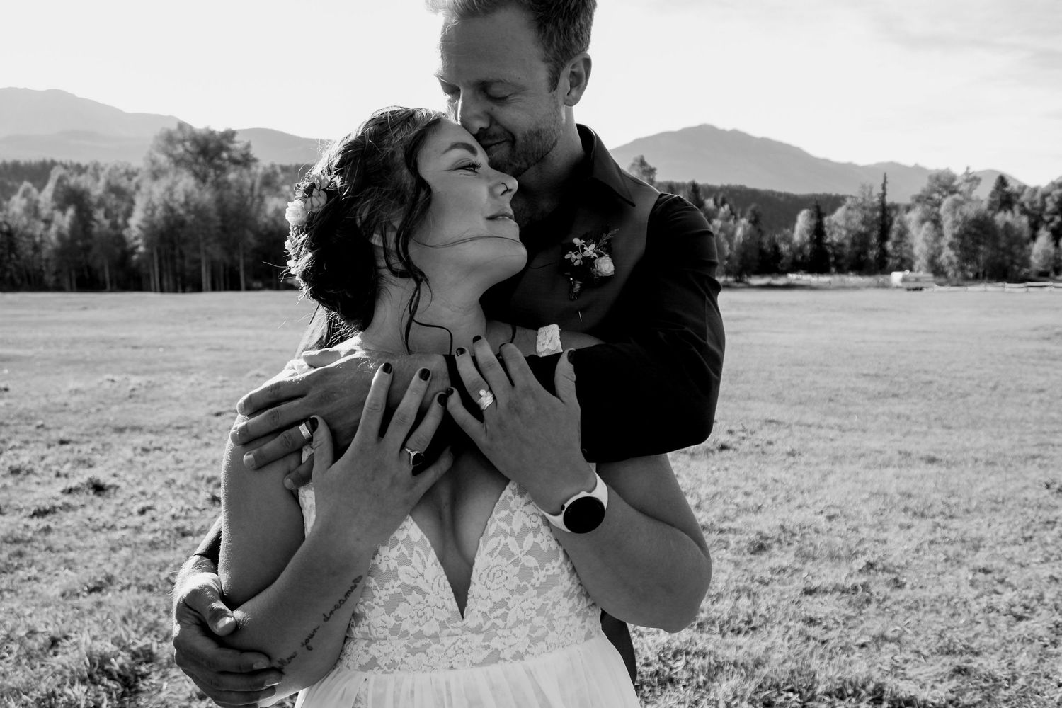A romantic black and white portrait of newlyweds embracing in a mountain field.