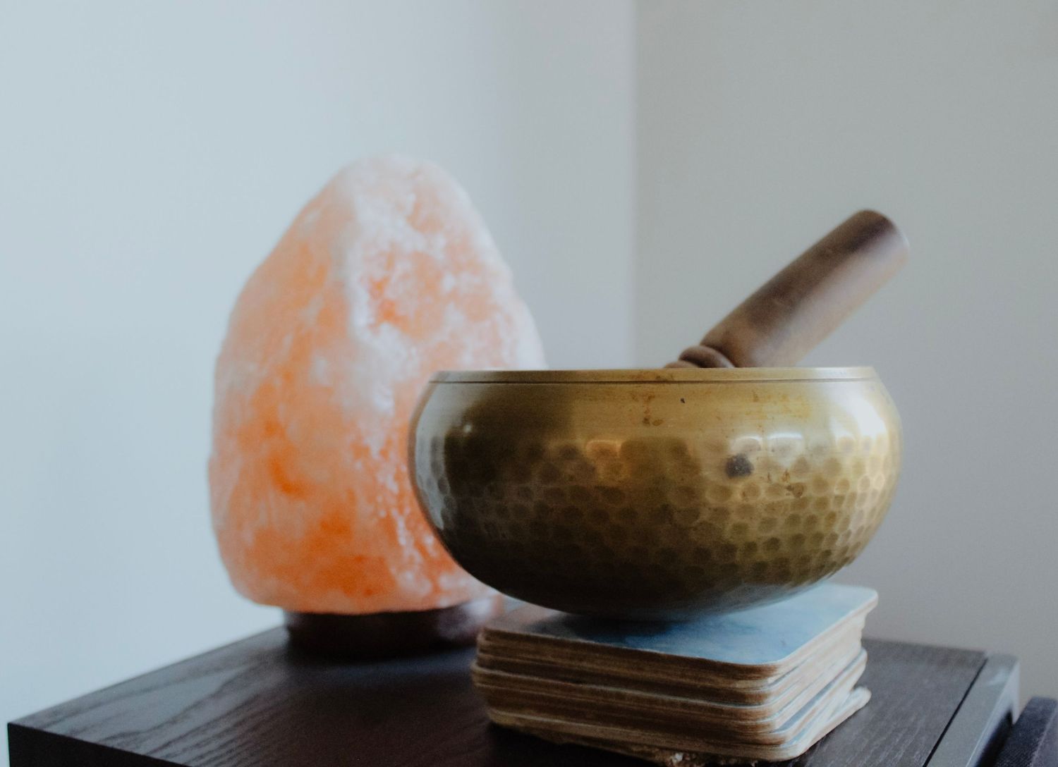 Meditation space with Himalayan salt lamp and singing bowl on dark wooden surface.