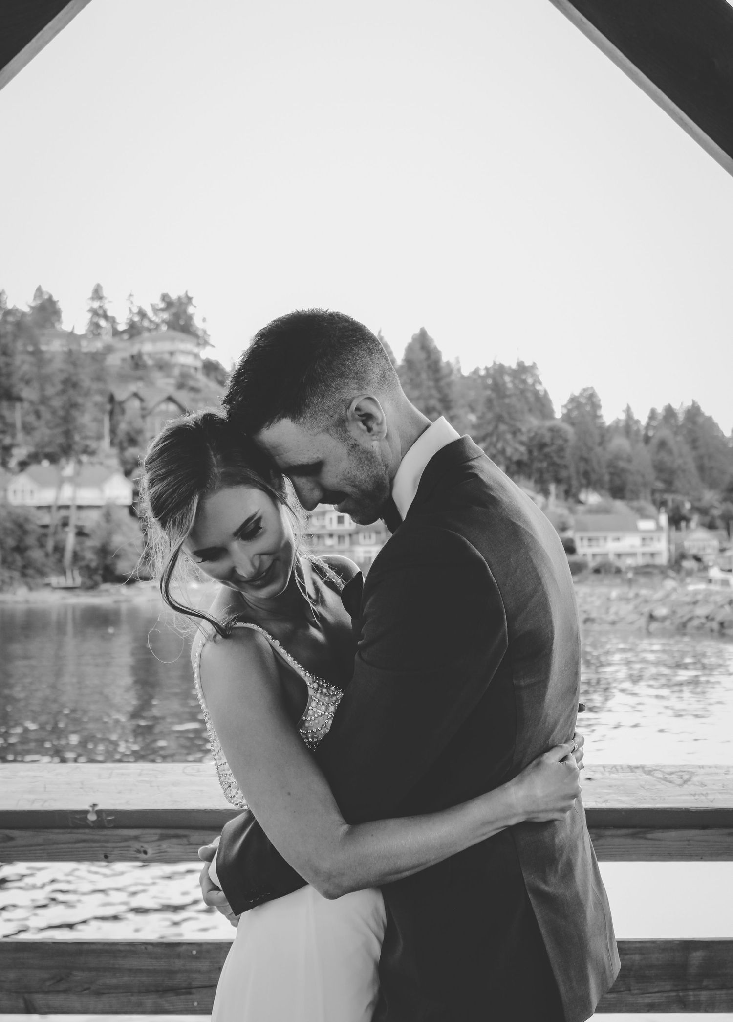Black and white wedding photography by a lakeside with mountains in background.