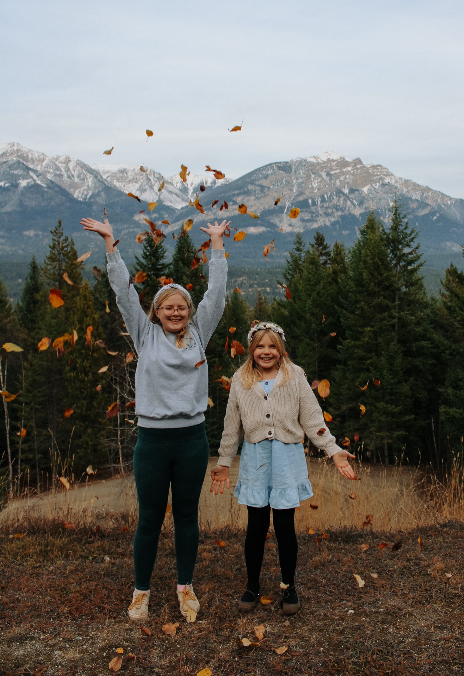 People throw autumn leaves in the air while celebrating in front of mountain scenery.