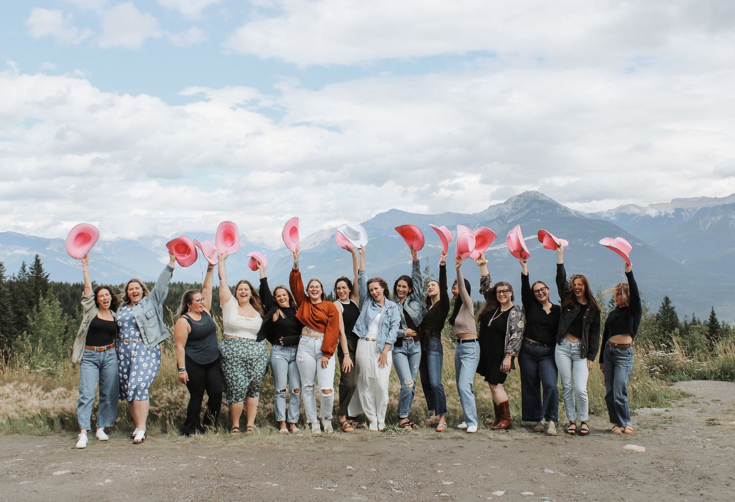 Group of women celebrating outdoors in mountains, waving pink and red fans against a cloudy sky backdrop.