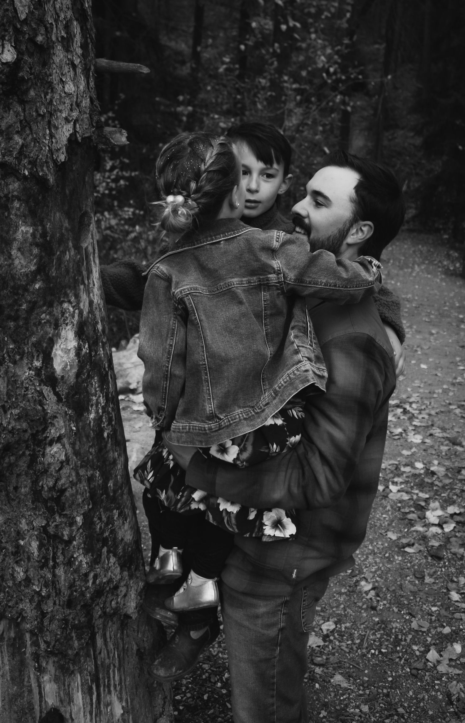 Artistic black and white portrait among tree trunks in a moody forest setting.
