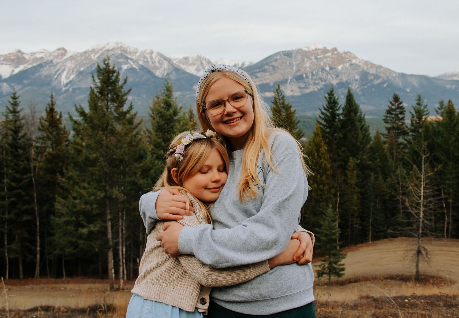 Two people embrace with mountains and evergreen forest creating a stunning backdrop.