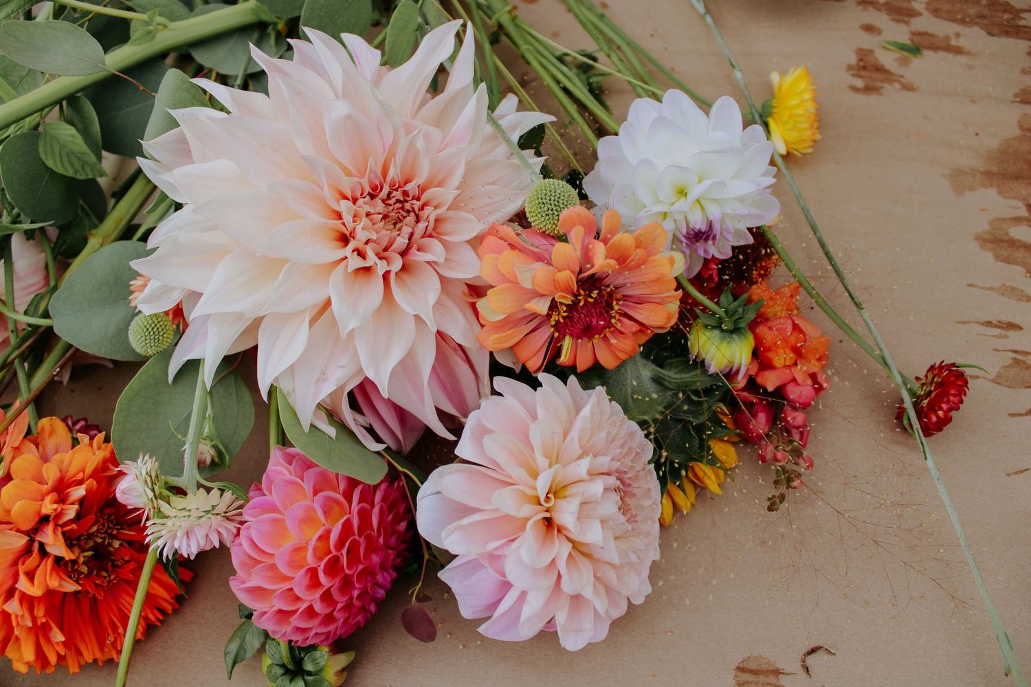 Beautiful arrangement of pink and peach dahlias with greenery on a wooden table.