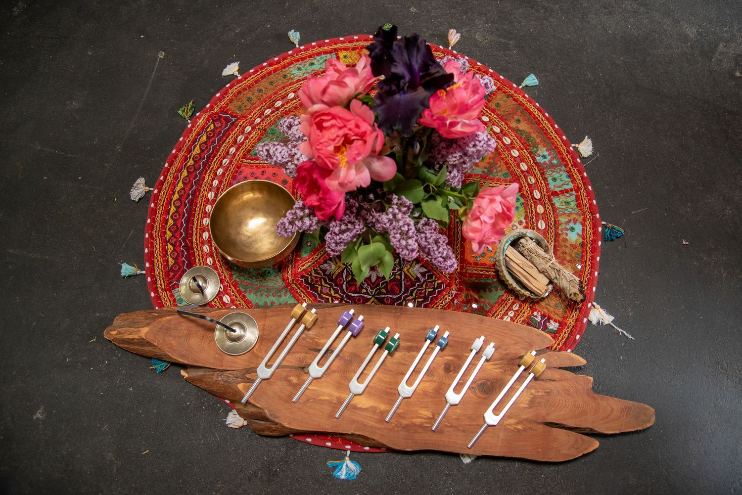 Decorative altar with pink flowers, brass bowl, tuning forks, and crystals on embroidered red mat.